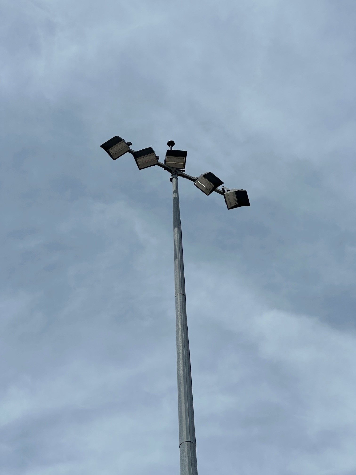 Tall stadium light pole with several floodlights against a cloudy sky