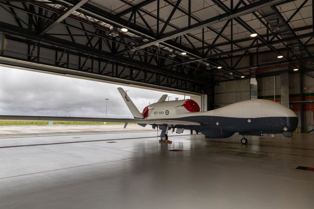 Jet aircraft parked in a hangar, viewed from the front-left side on a wet concrete floor.