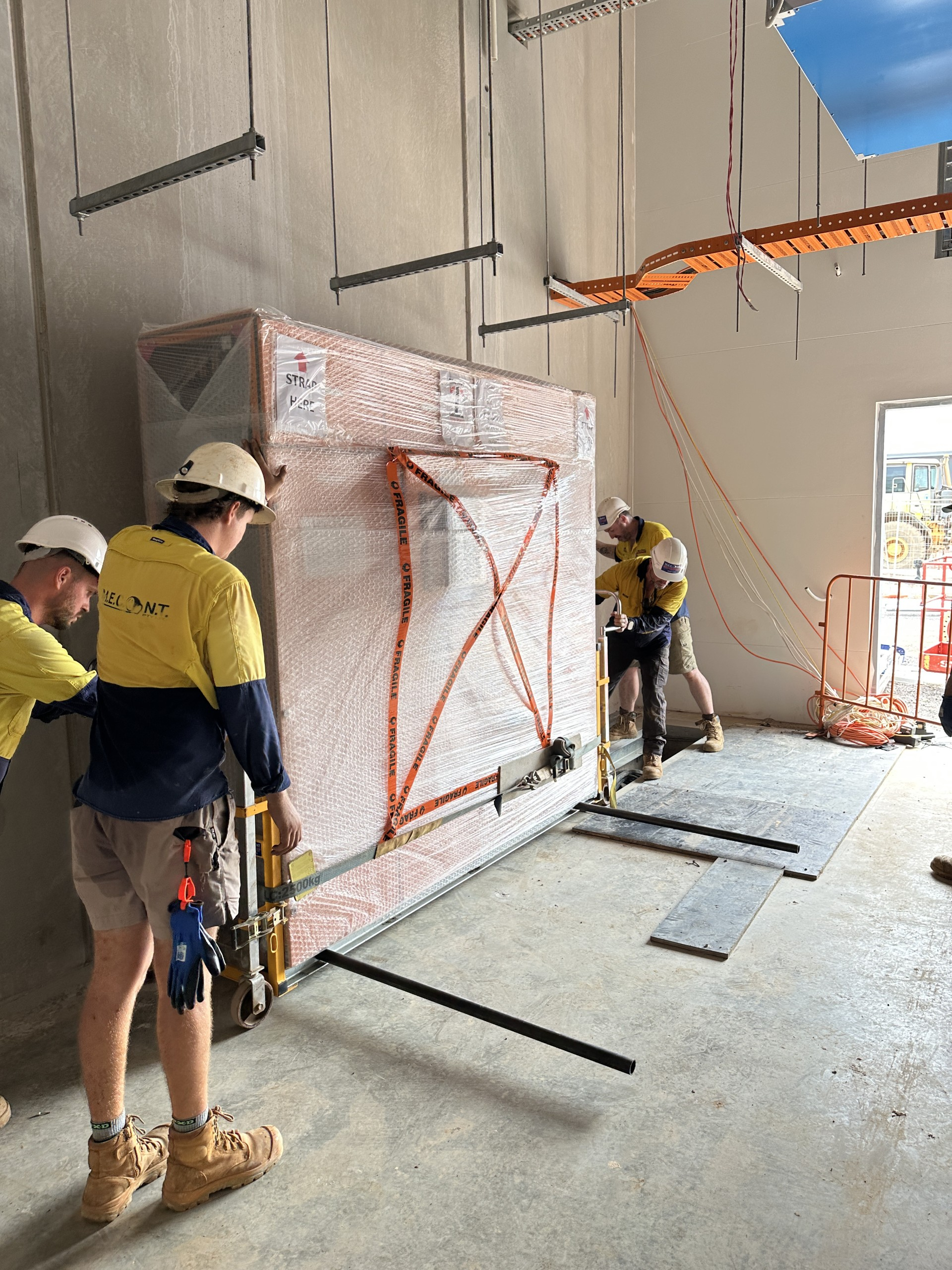 Workers in hard hats moving a large wrapped panel inside a construction site