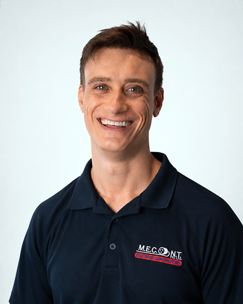 Smiling man in a navy polo shirt with a company logo, standing against a light background.