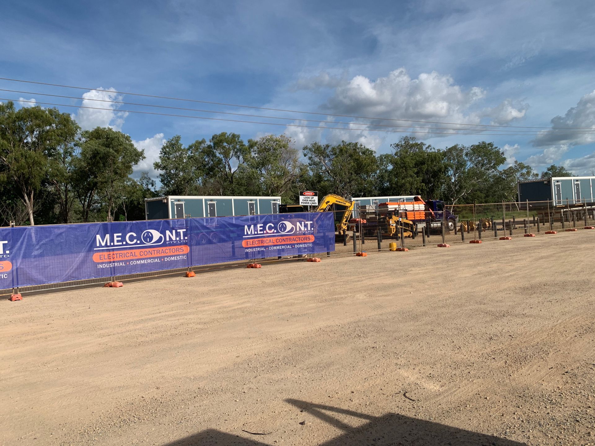 Outdoor worksite with blue fencing, construction equipment, and workers under a cloudy sky