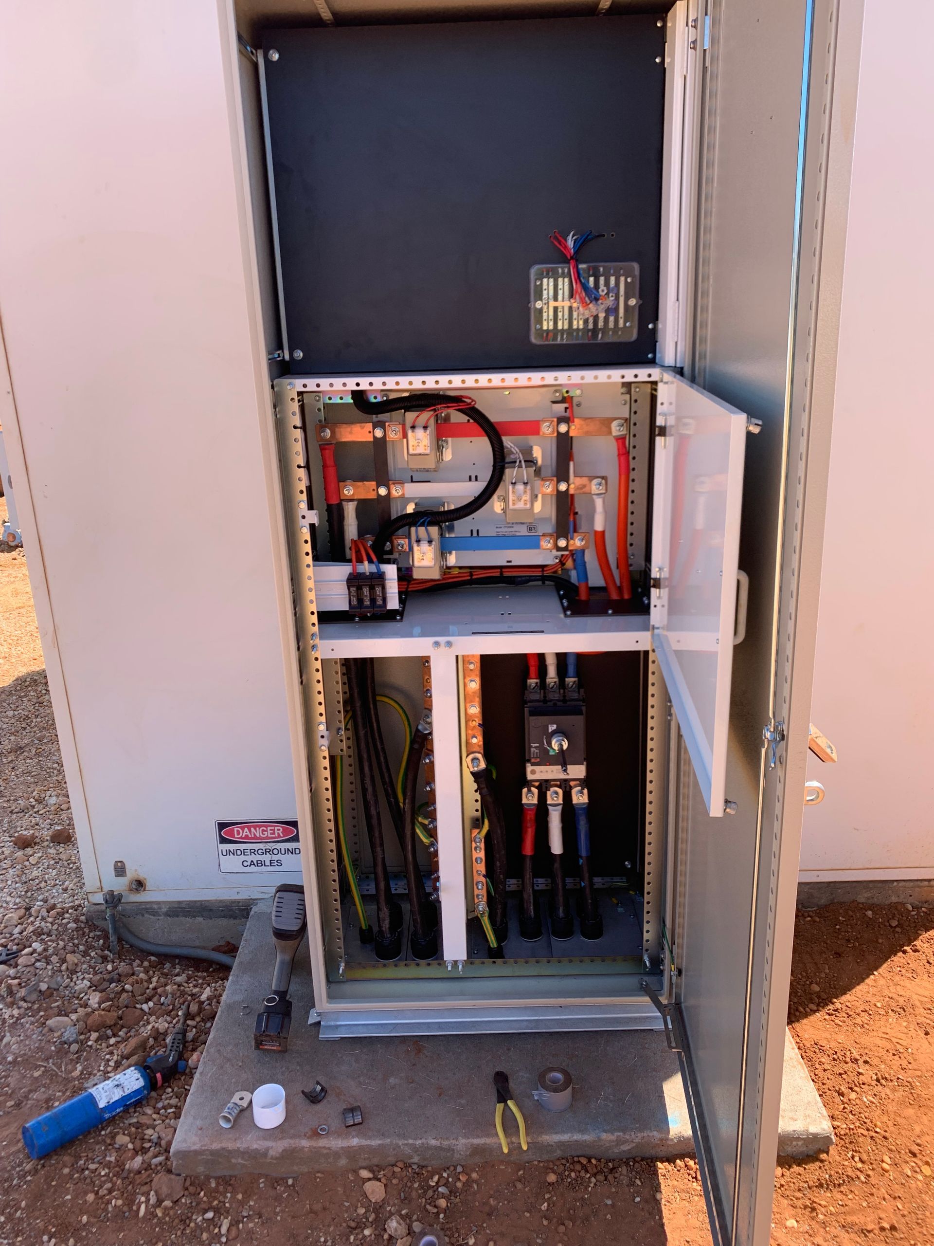Open electrical cabinet with exposed wiring, breakers, and components on a utility panel.