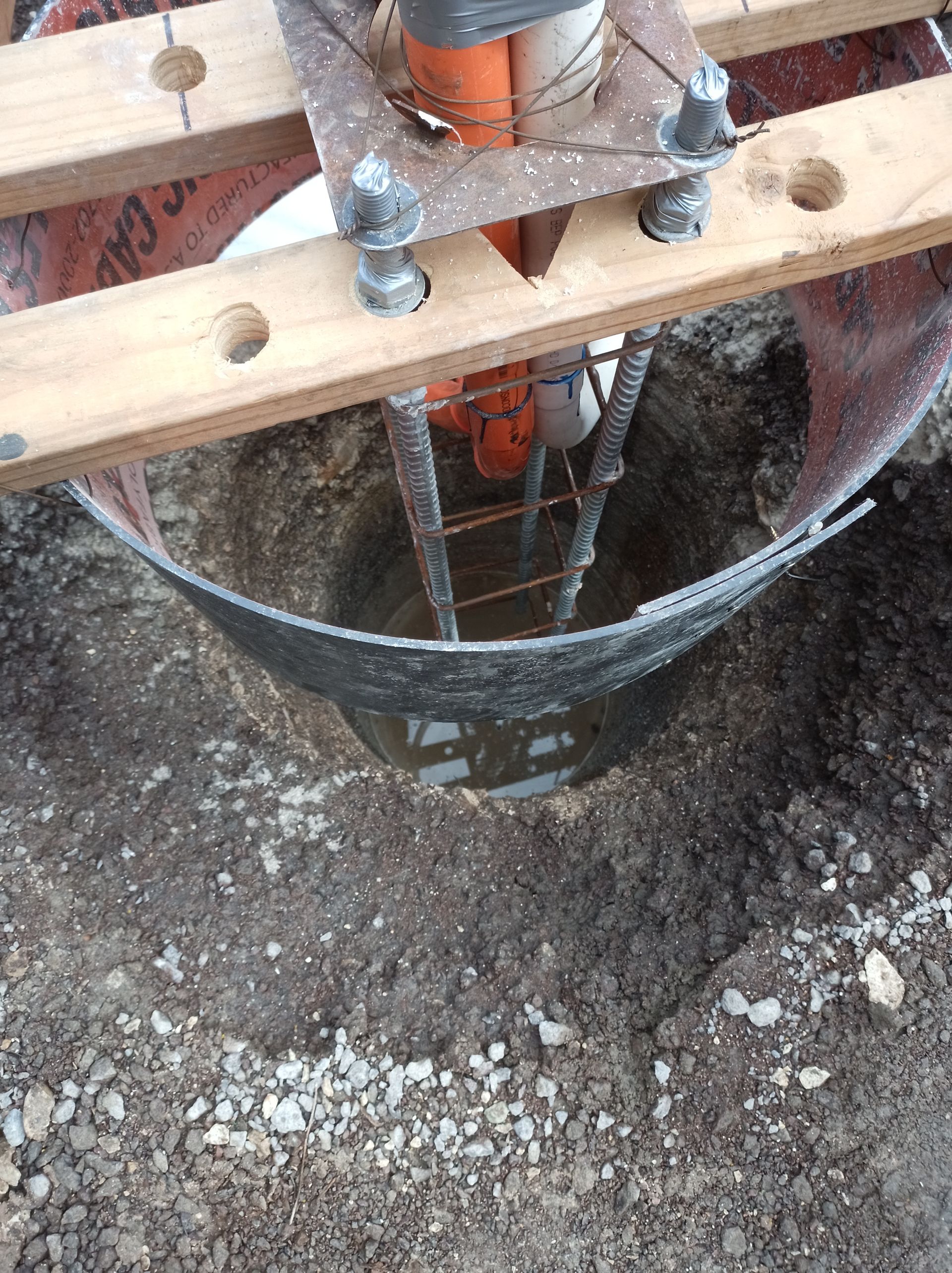 Construction site hole with rebar cage and wooden planks over concrete ground