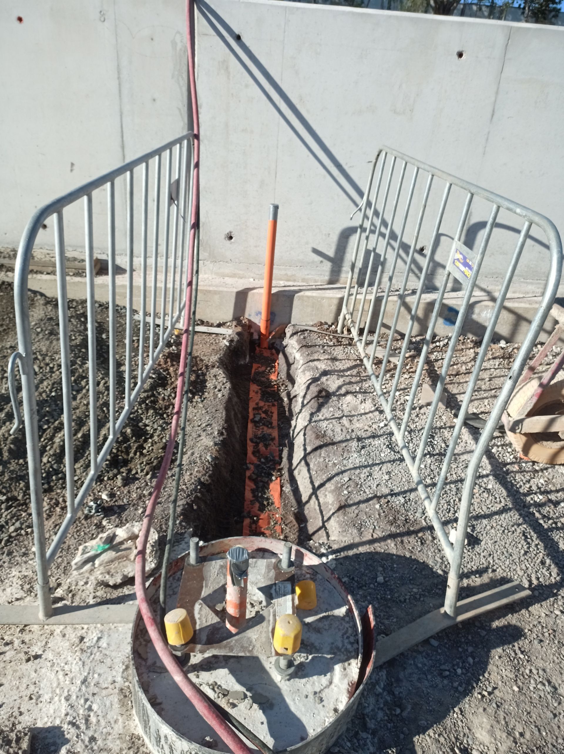 Damaged walkway beside a wall, with bent metal railings and exposed ground around a central trench.