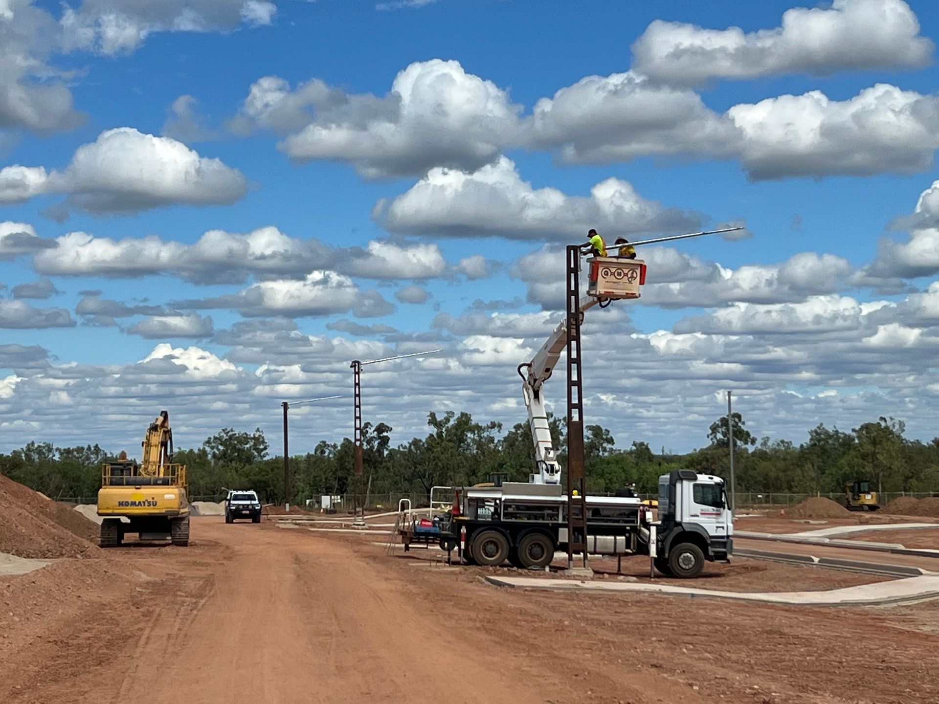 Construction vehicles grading a dirt road under a cloudy sky.