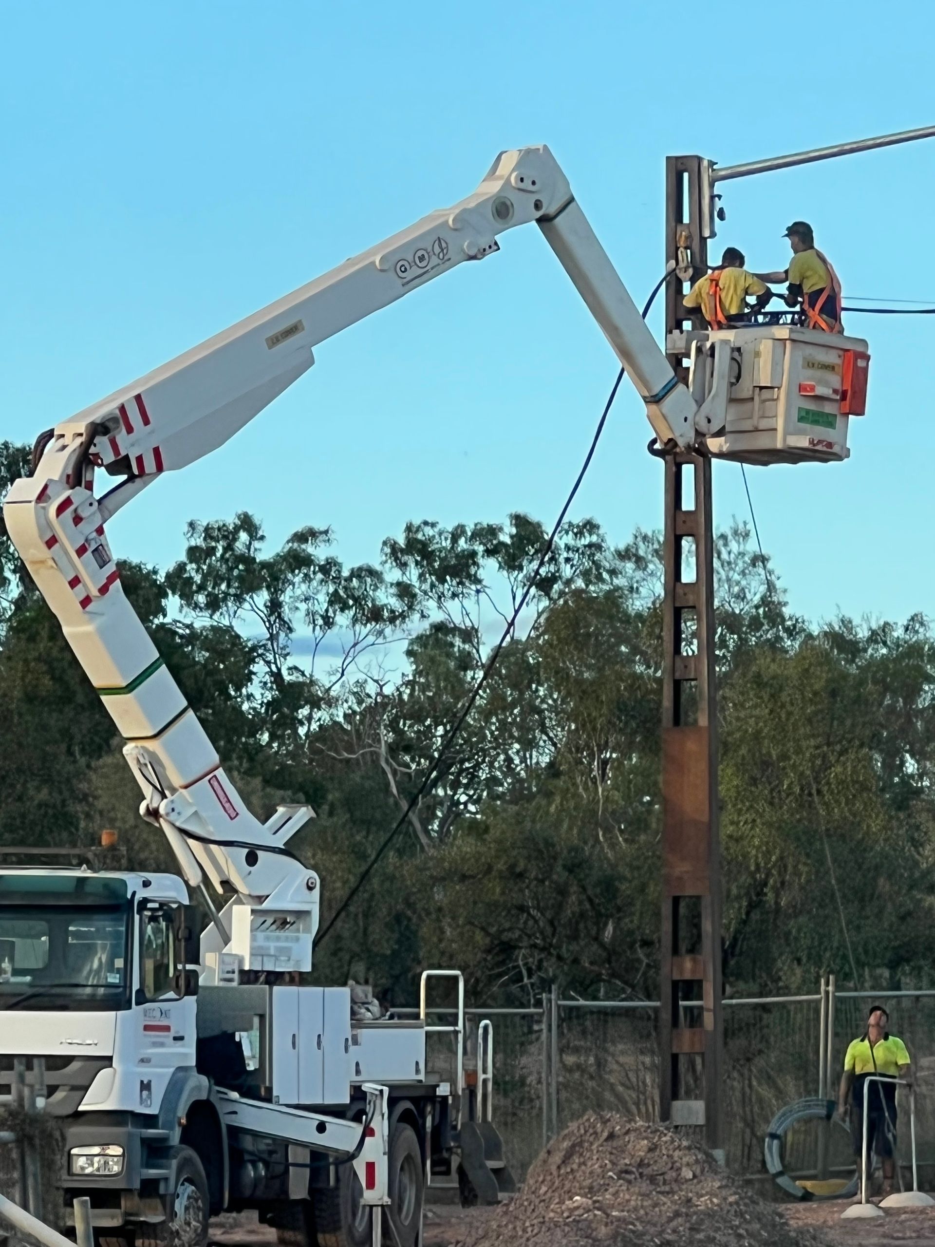 Workers in a bucket lift installing a pole beside a truck at a construction site.