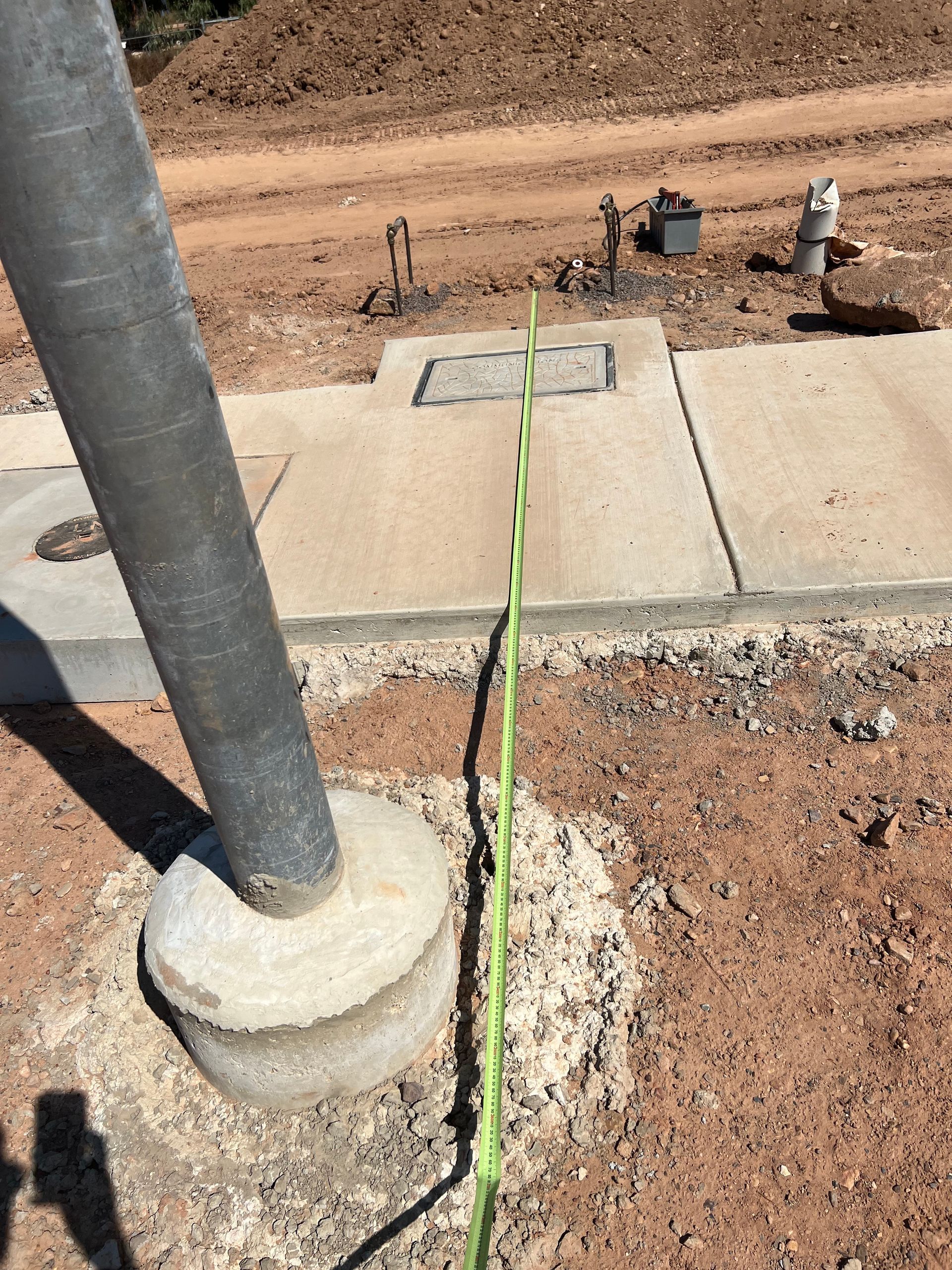 Green tape measures a gap in a concrete sidewalk beside a utility pole at a construction site