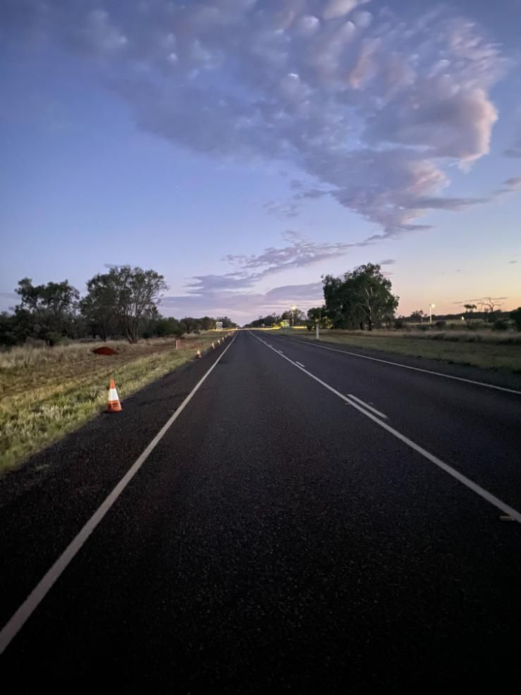 Empty rural road at dusk with a cloudy sky and orange traffic cones along the shoulder