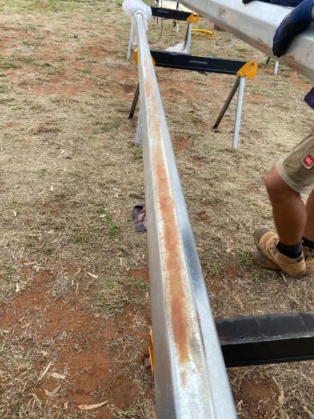 Long metal beam on stands outdoors with a person’s leg visible at right