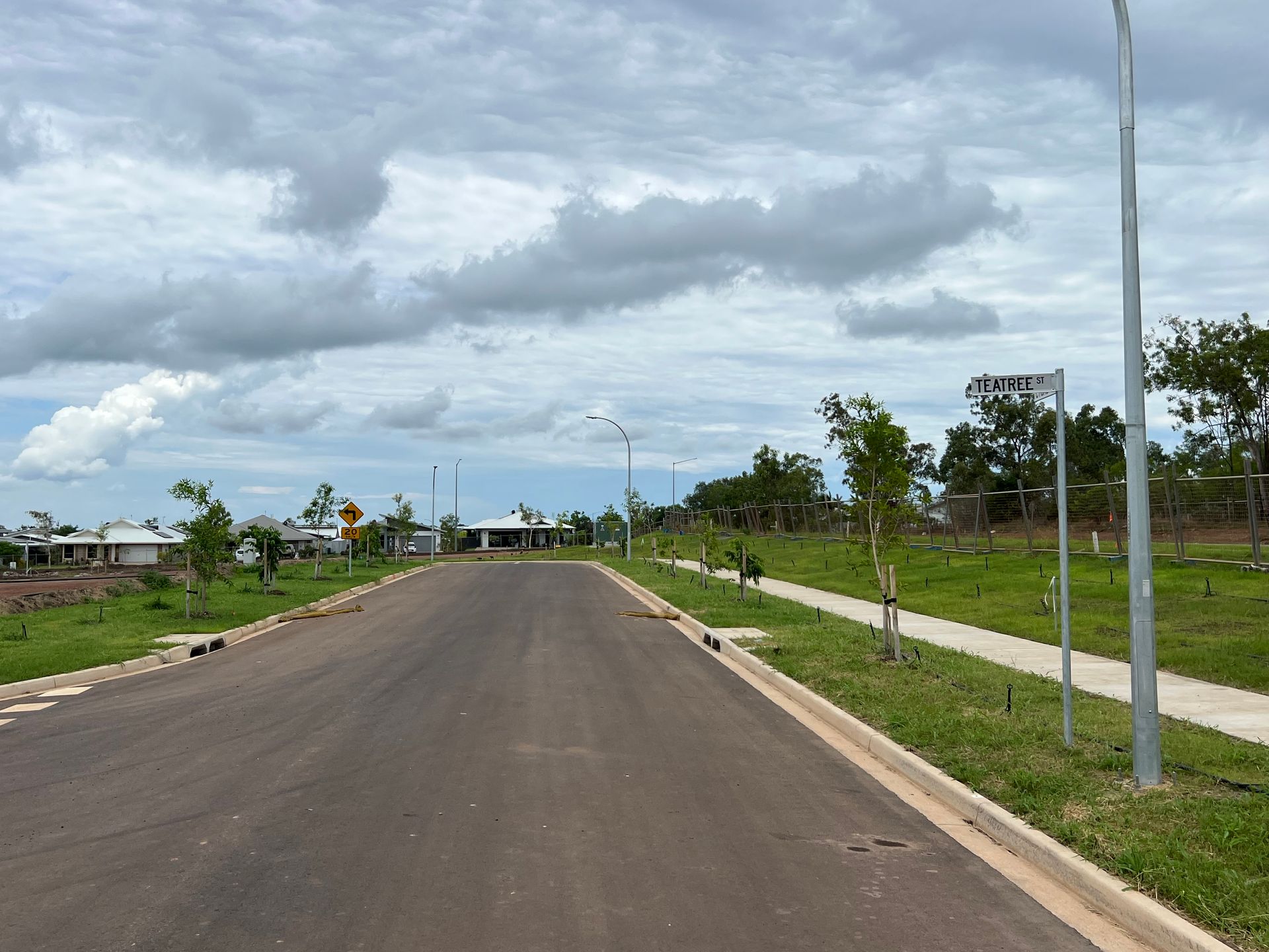 Empty paved road through a grassy residential area under a cloudy sky