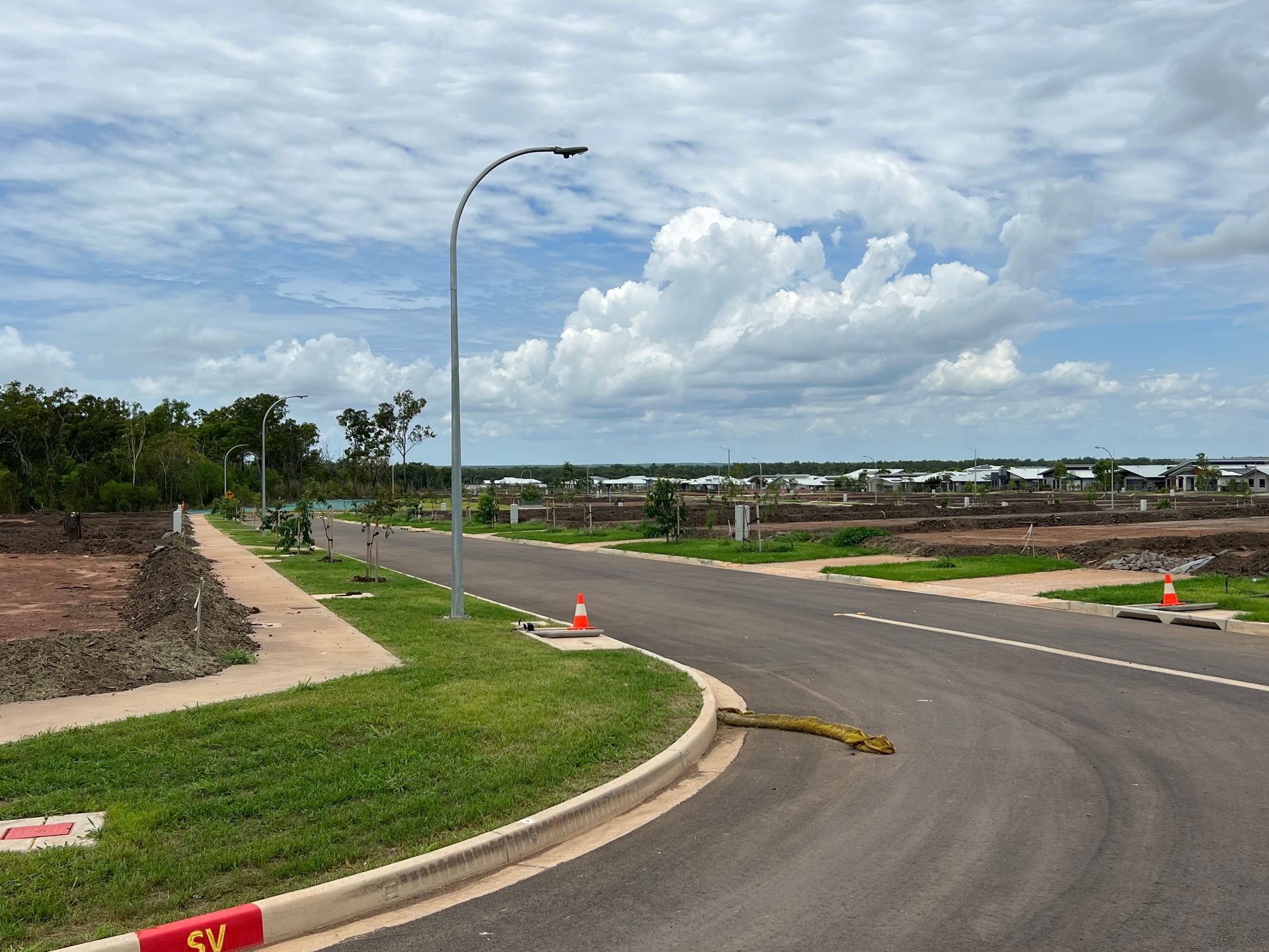 Curving road in a new residential area under a cloudy sky, with streetlights and traffic cones.