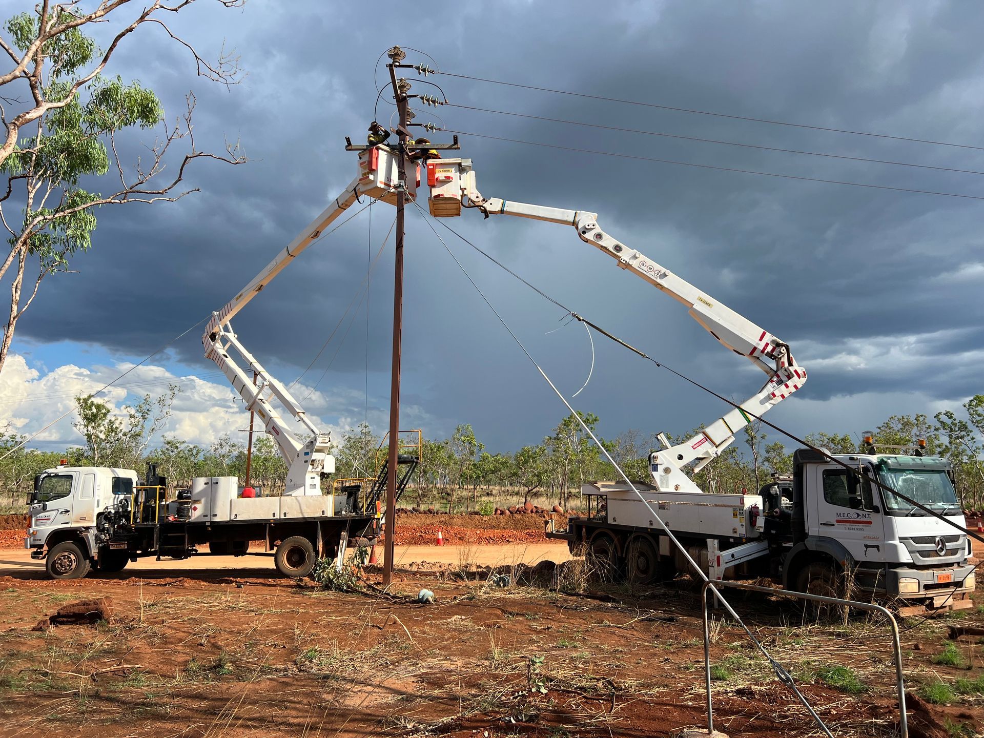 Two bucket trucks with extended booms working on a utility pole under stormy skies.
