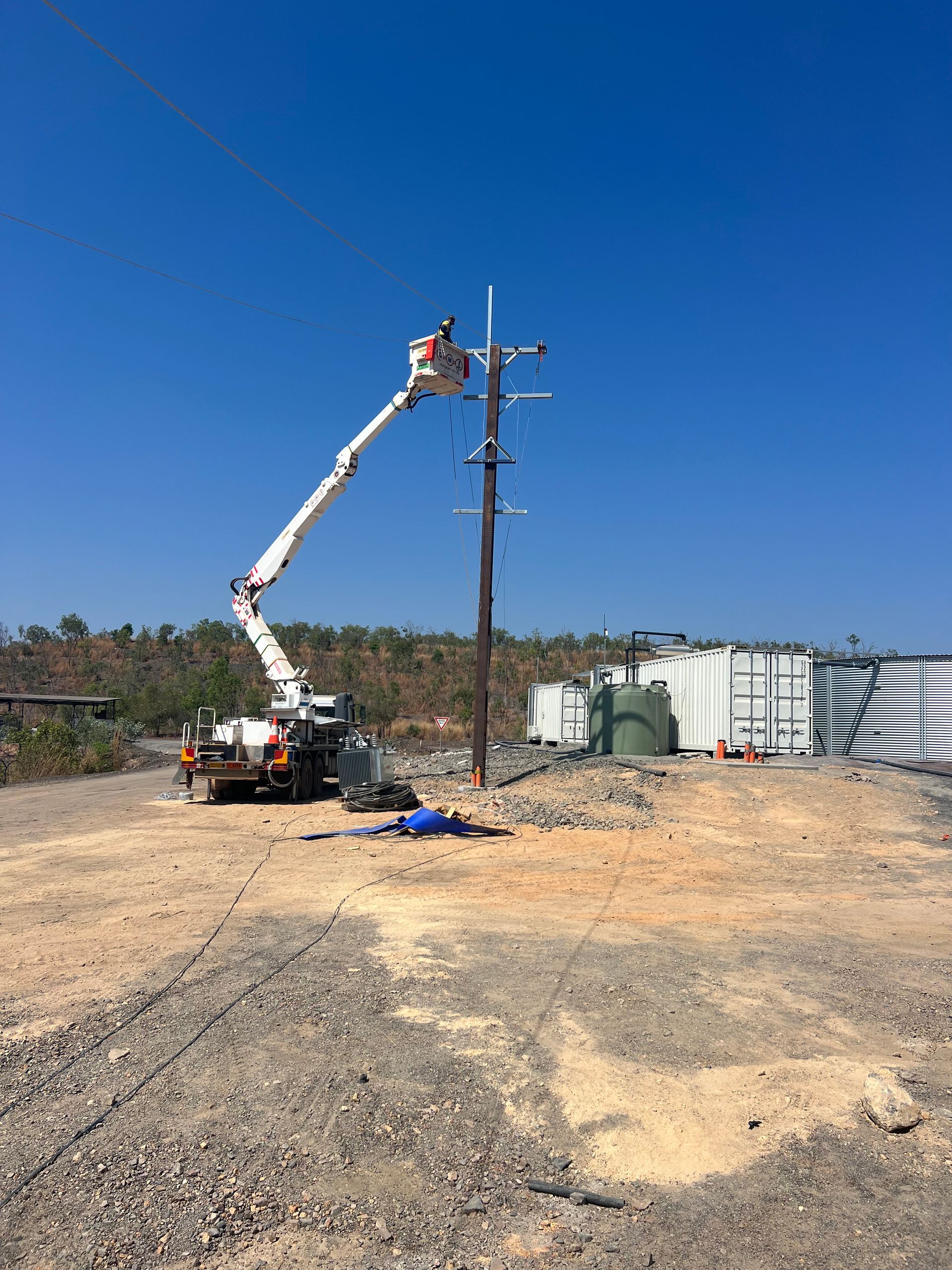 Utility worker in a bucket lift repairing power lines beside a utility pole on a dusty lot