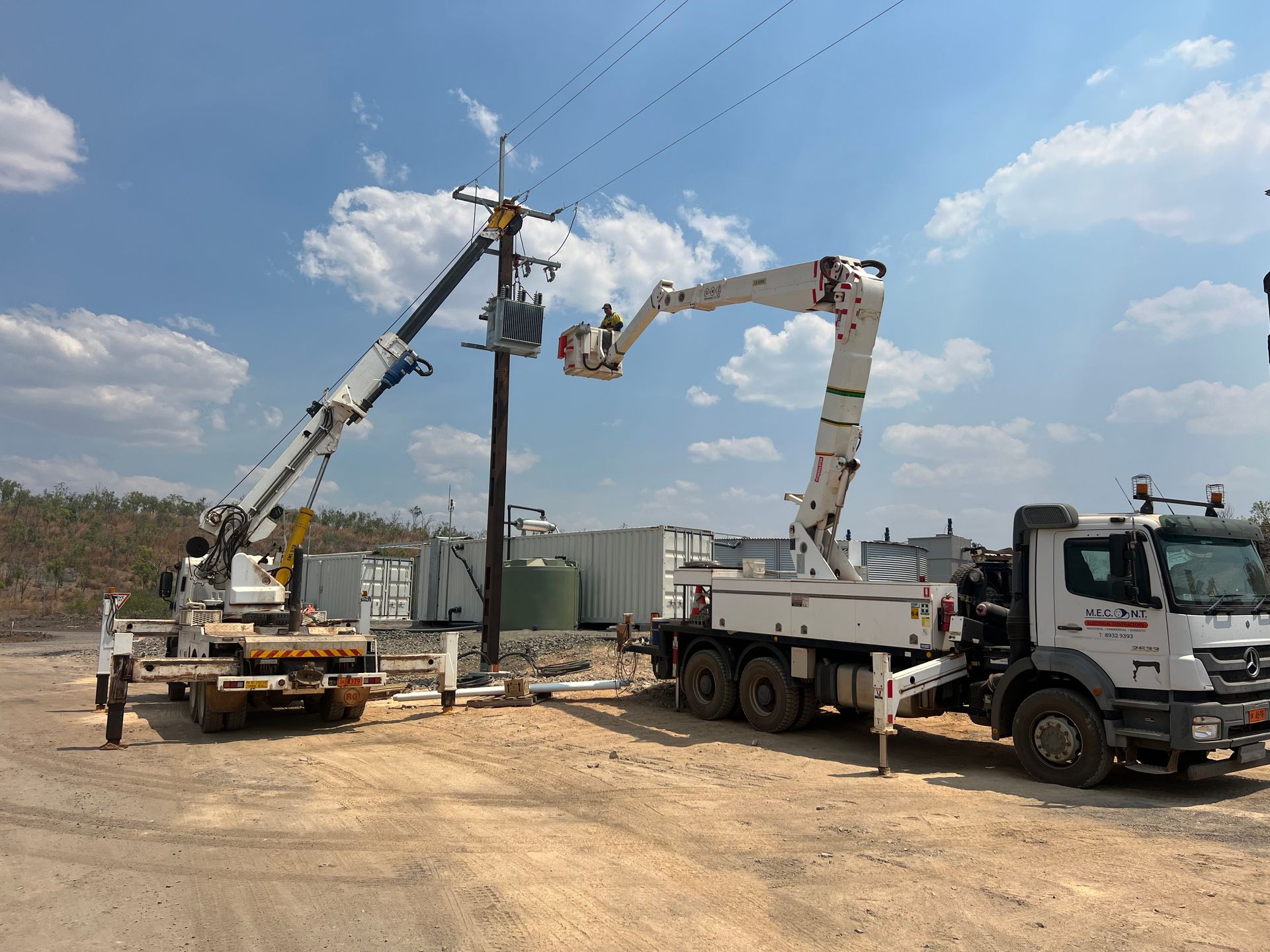 Two utility trucks with bucket lifts working on power lines under a blue sky