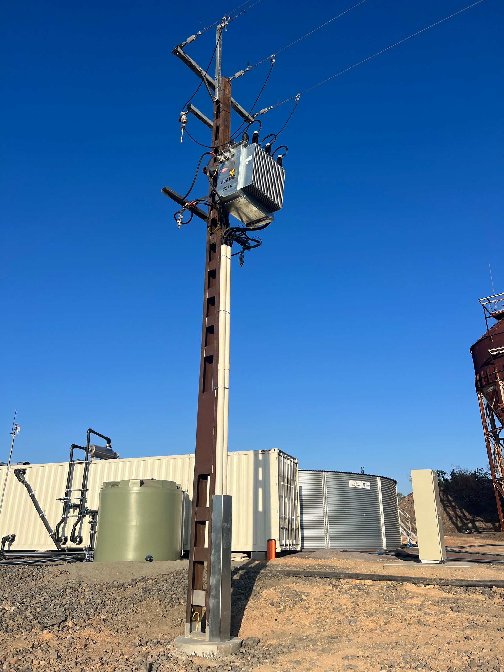 Utility pole with transformer and power lines in a dry industrial lot under a clear blue sky