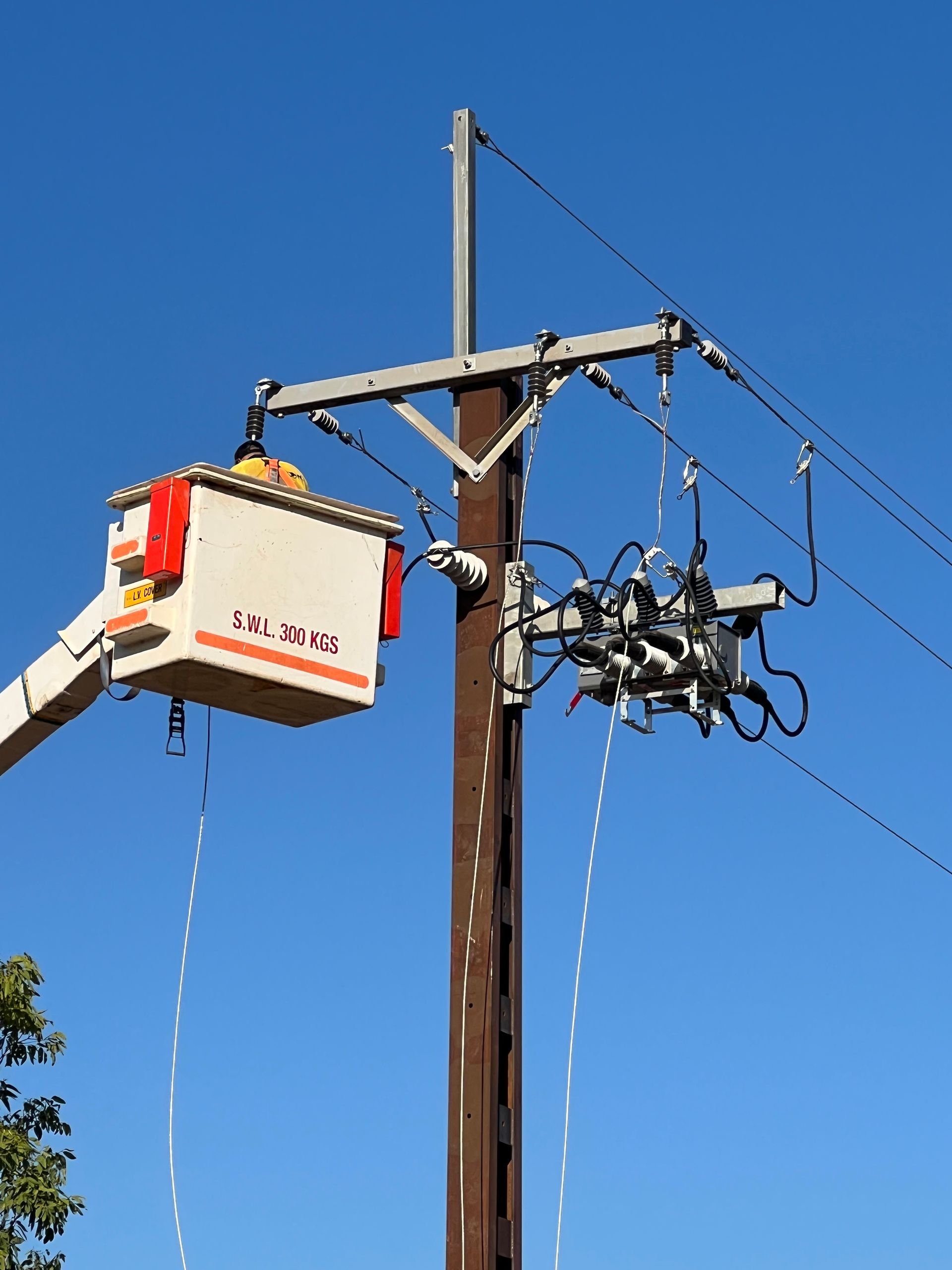 Utility worker in bucket truck repairing power lines on a wooden utility pole under a clear blue sky