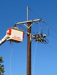 Utility crew in bucket truck working on a power pole and electrical lines against a blue sky