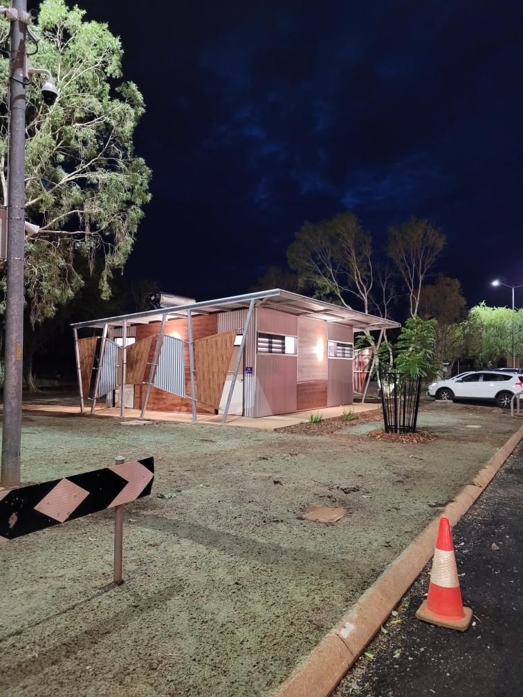 Nighttime view of a small pink building with lights, trees, and a white car parked nearby