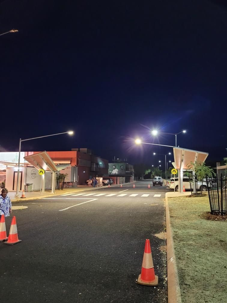 Nighttime road entrance with streetlights, orange cones, and a pedestrian crossing near buildings