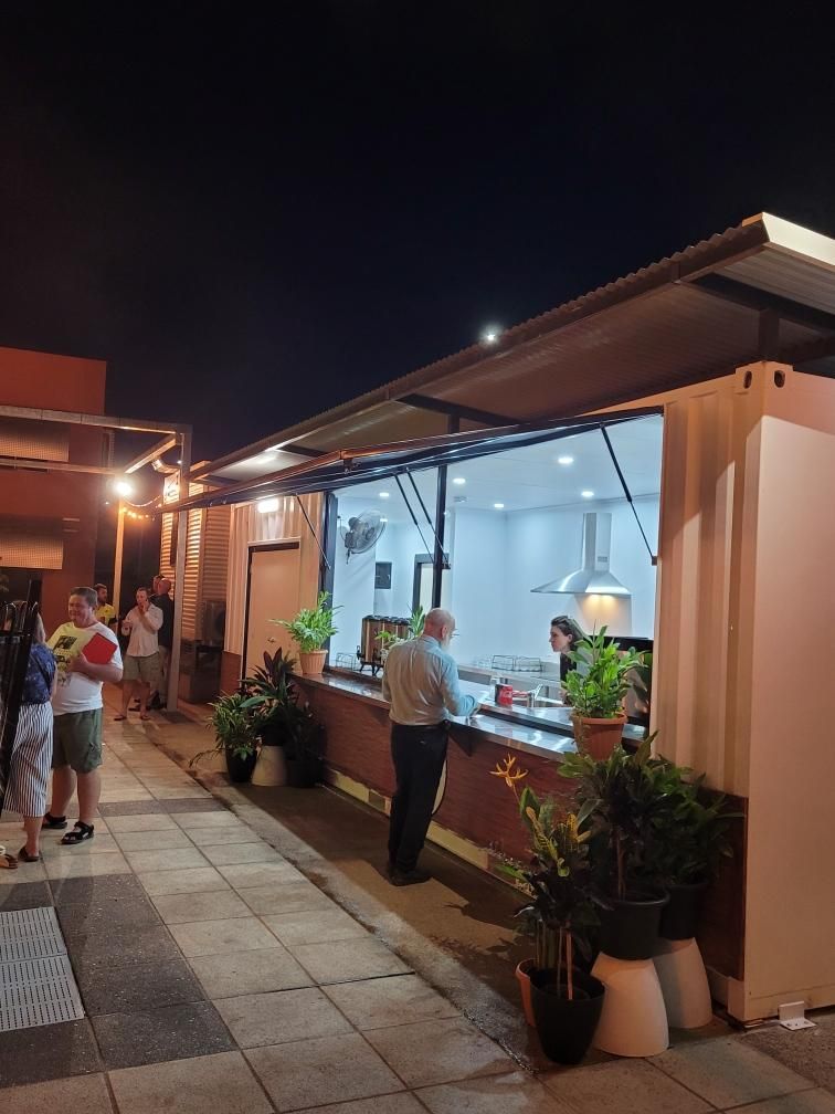 Nighttime outdoor market with people browsing and a lit food stall under a canopy