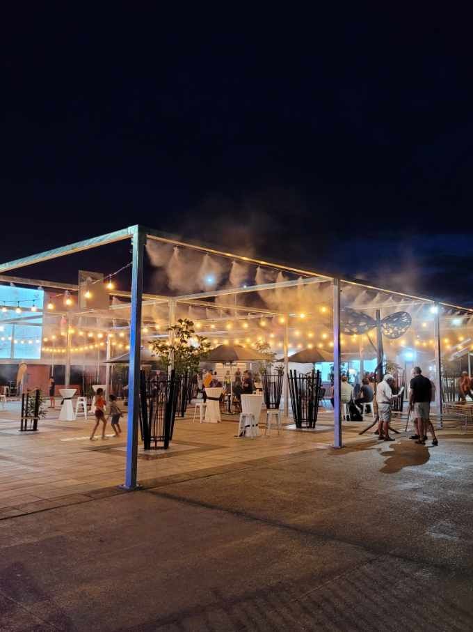 Outdoor nighttime event under string lights with people mingling in a tented plaza