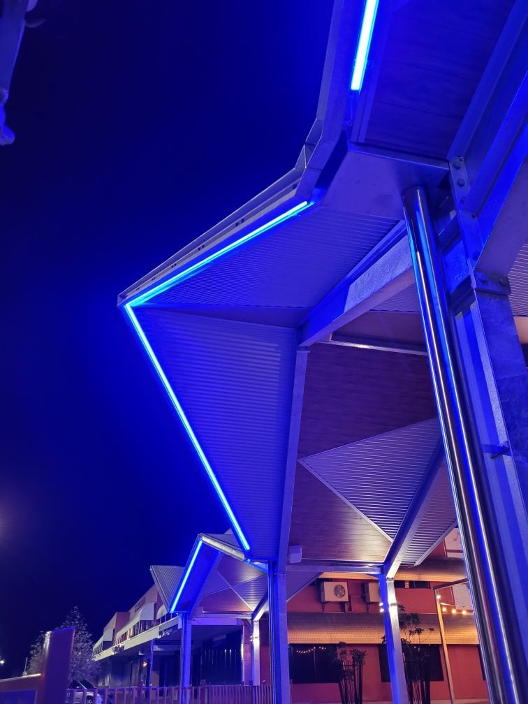 Blue neon-lit modern canopy structure at night with angular rooflines and columns