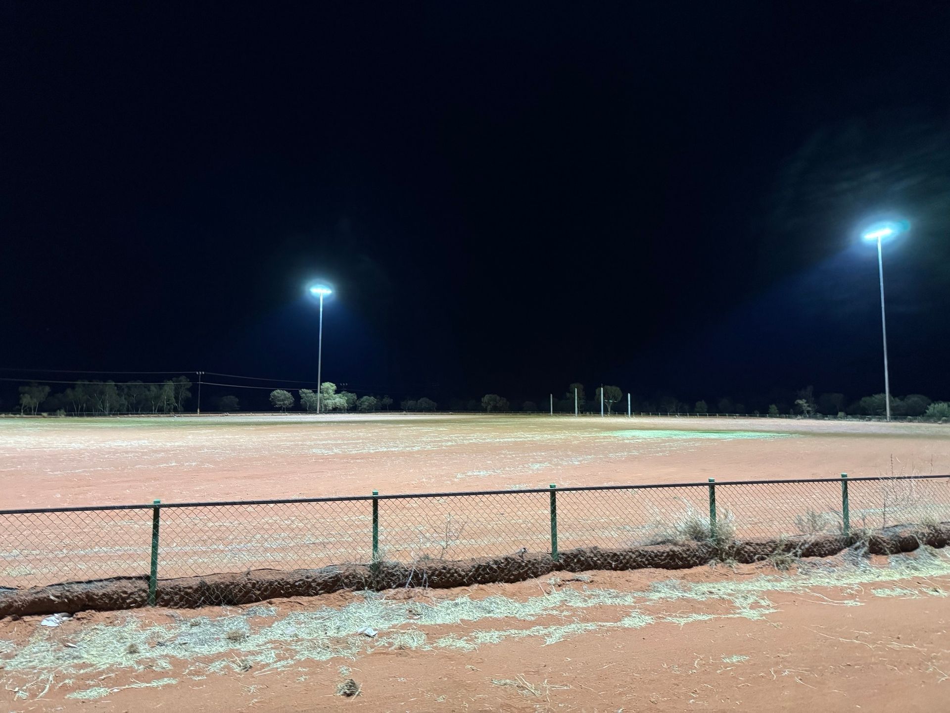 Empty lit sports field at night with a chain-link fence in the foreground