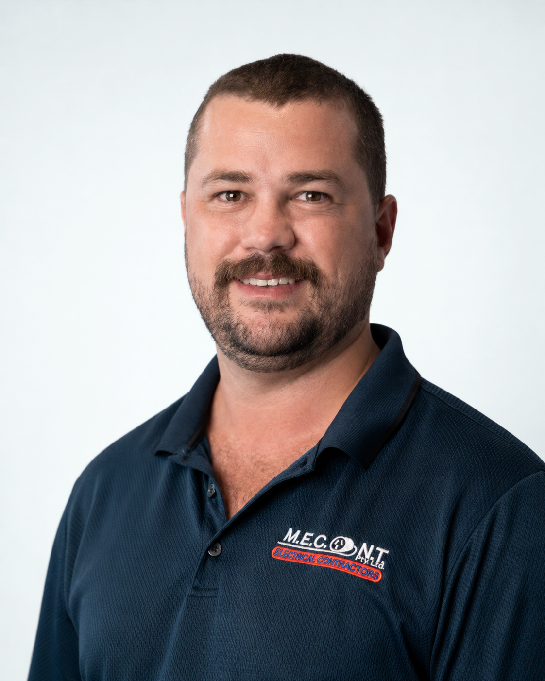 Portrait of a smiling man in a navy polo shirt with a company logo, against a light background