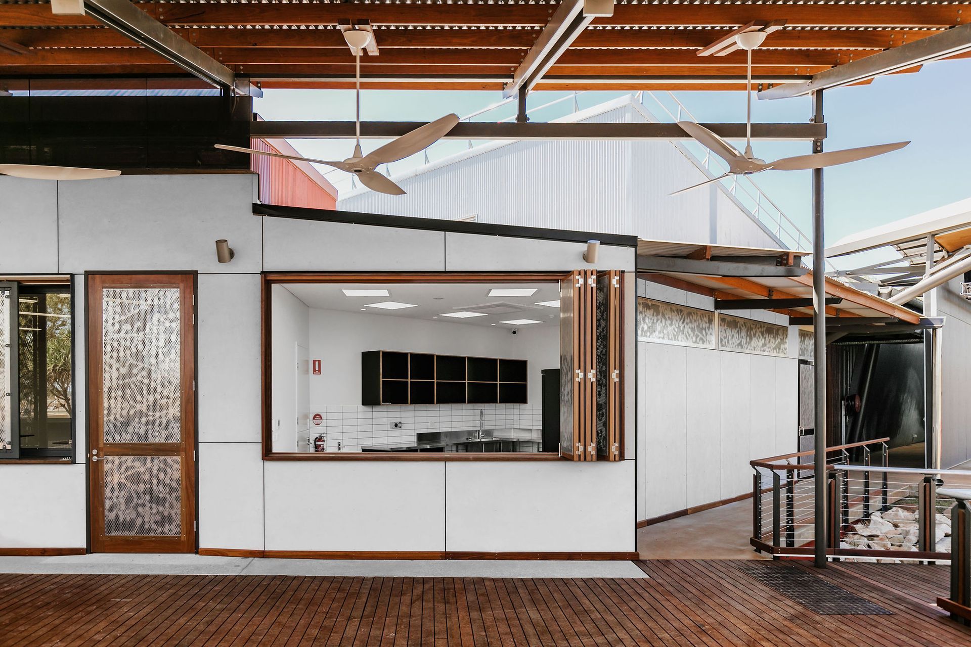 Modern open-air cafe with white walls, wood accents, and hanging ceiling fans