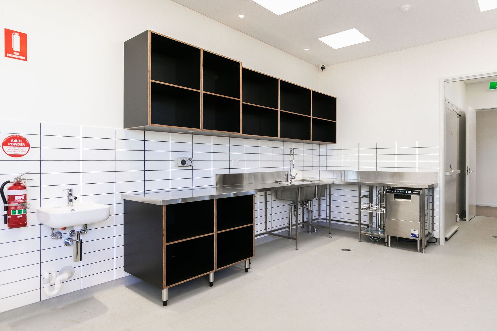 Bright hospital or lab room with white walls, black cabinets, sink, and metal work tables