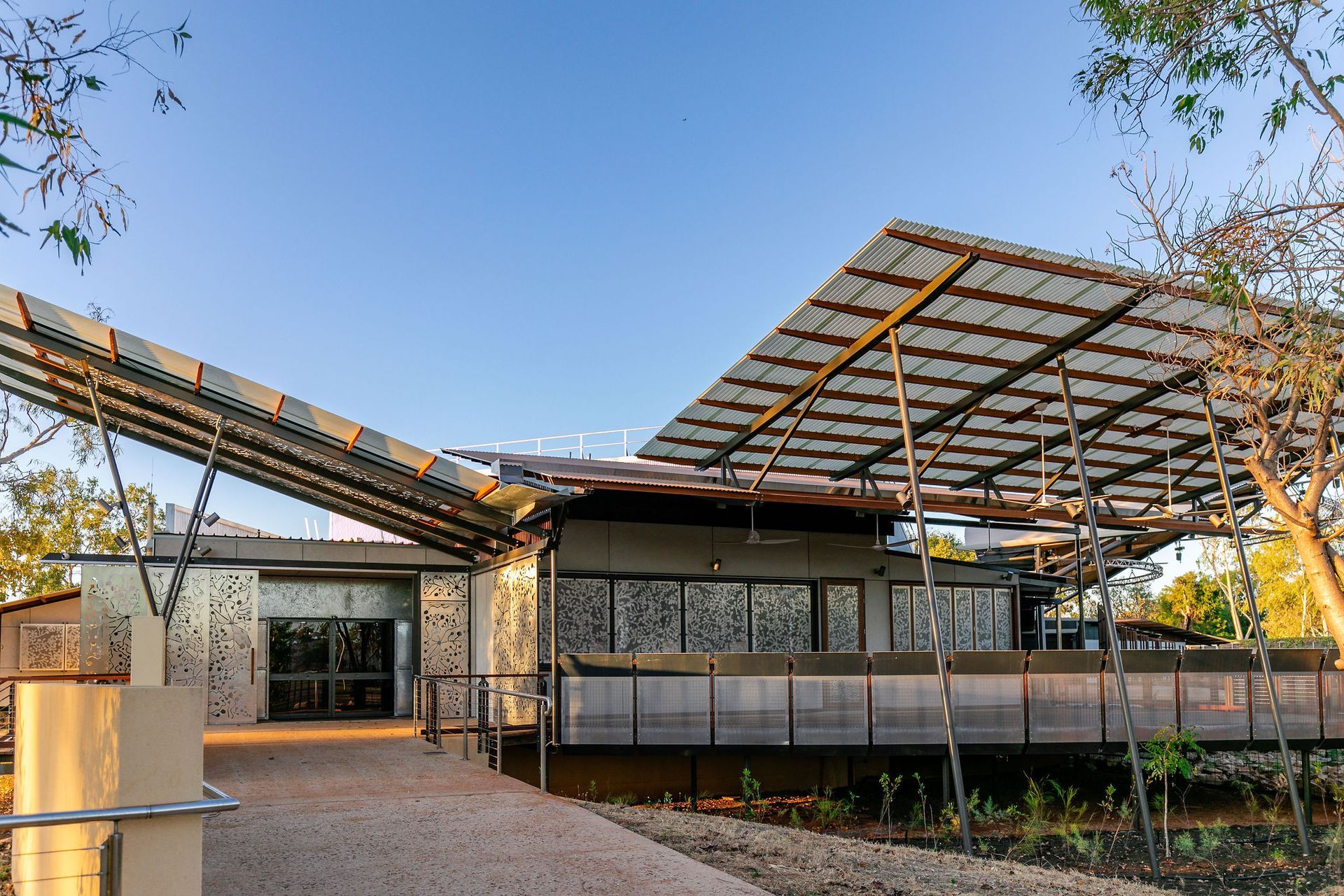 Modern house with glass walls and a large solar-panel canopy in a landscaped courtyard