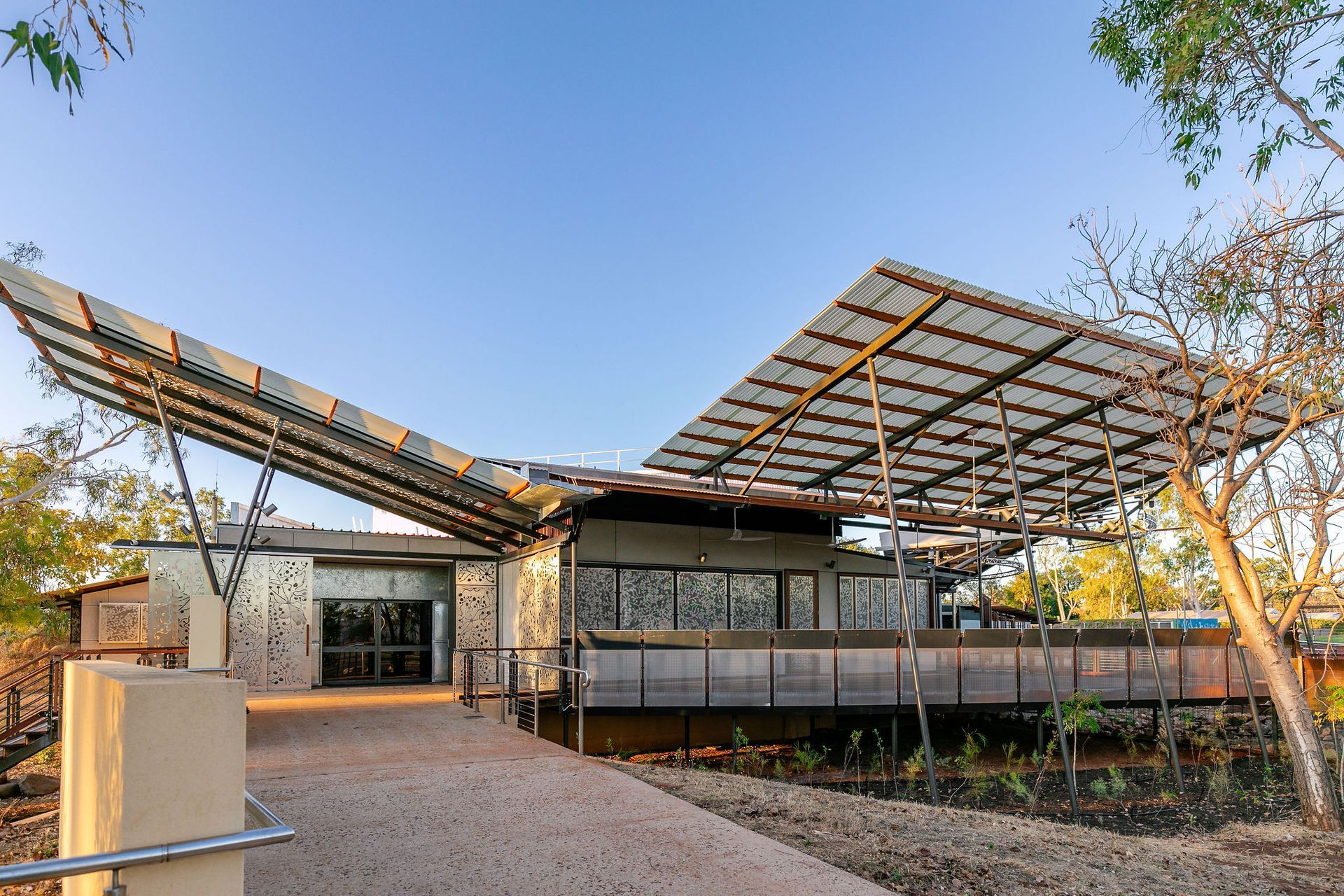 Modern building with a large lattice roof and stone facade in a landscaped courtyard under a blue sky