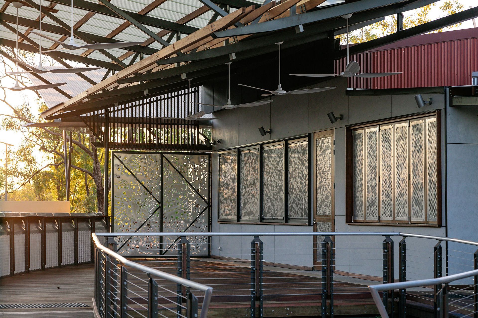 Covered outdoor patio with metal railings, large windows, and a corrugated roof at sunset