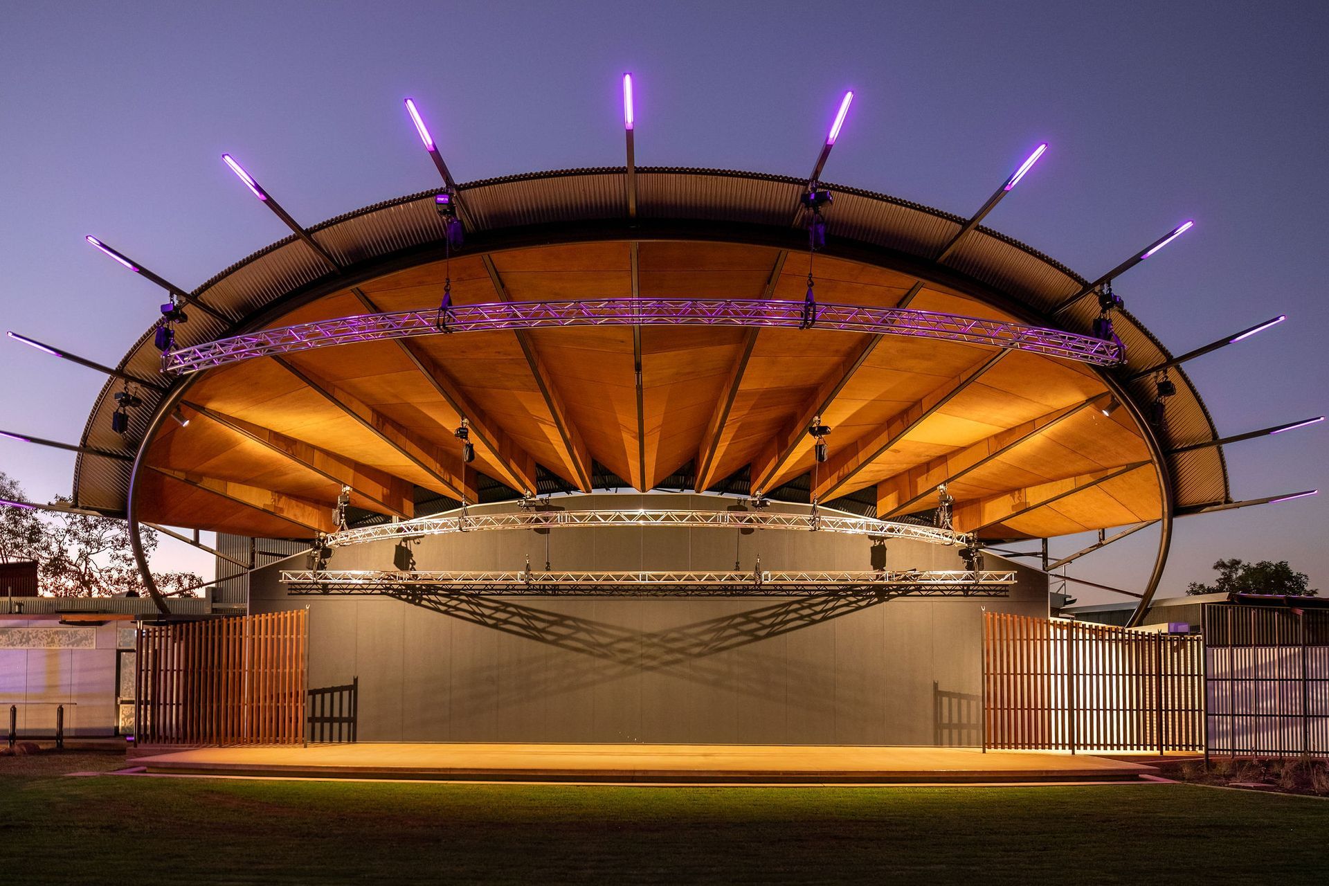 Illuminated outdoor stage with a large curved orange roof at dusk