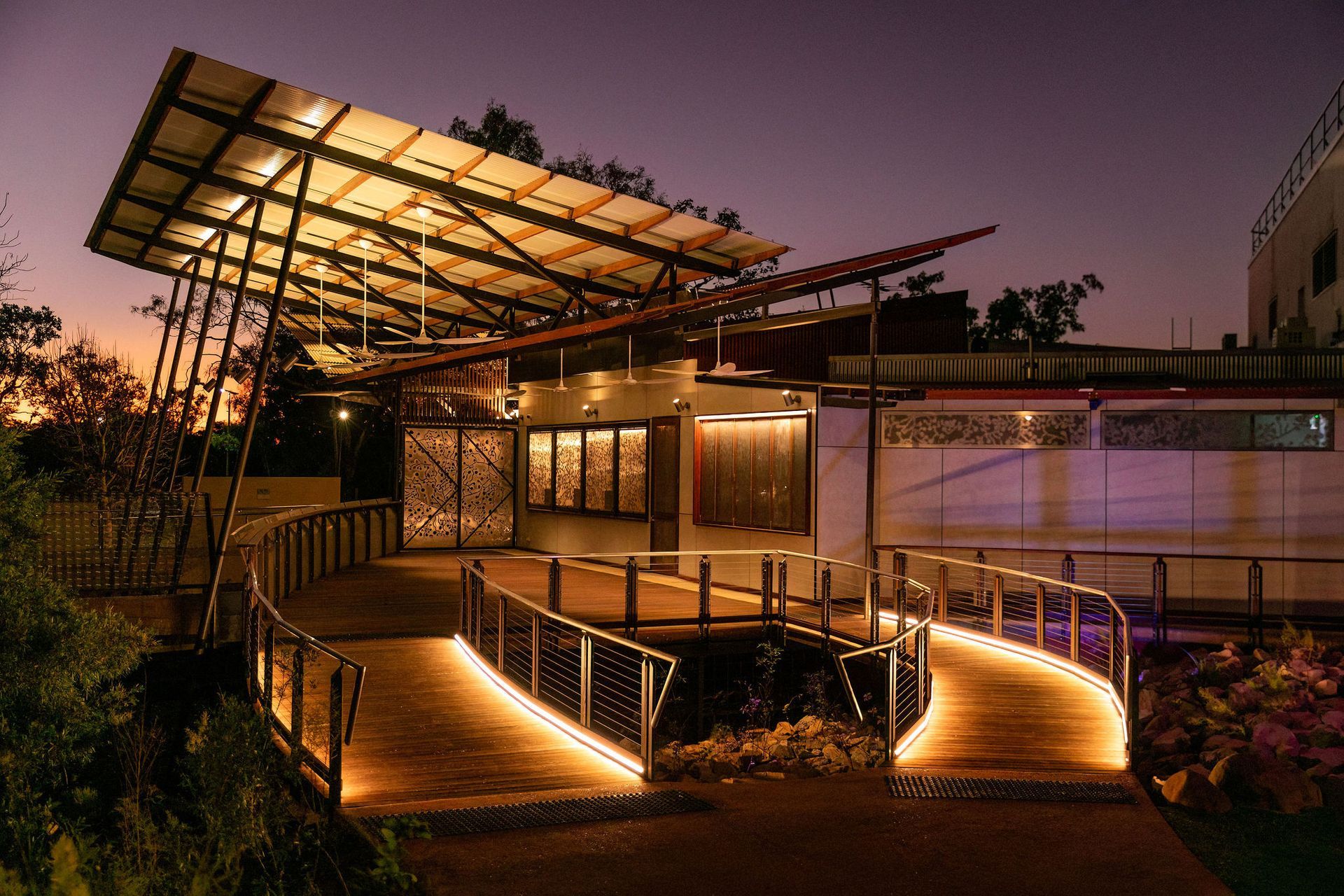 Modern building entrance at dusk with glowing pathway lights and a solar-panel canopy