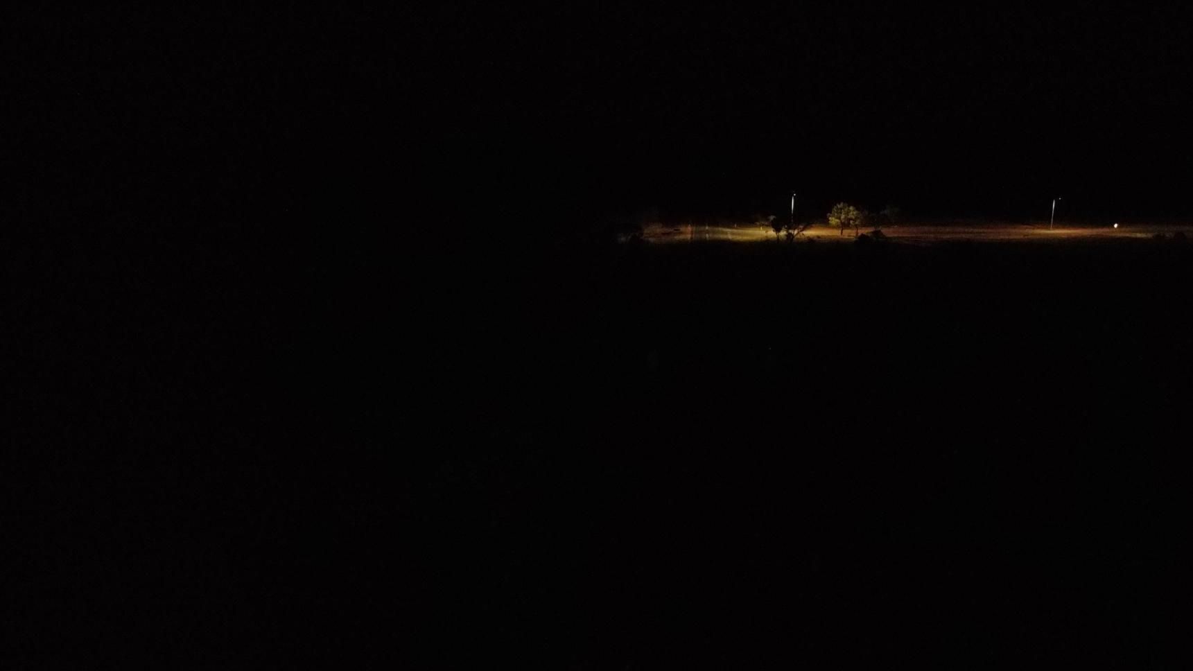 Dark night scene with a faintly lit shoreline or distant lights along the horizon
