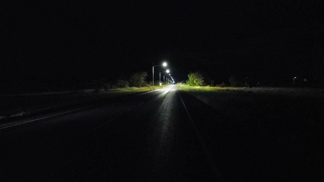 Dark road at night with distant streetlights and a bright glow on the horizon