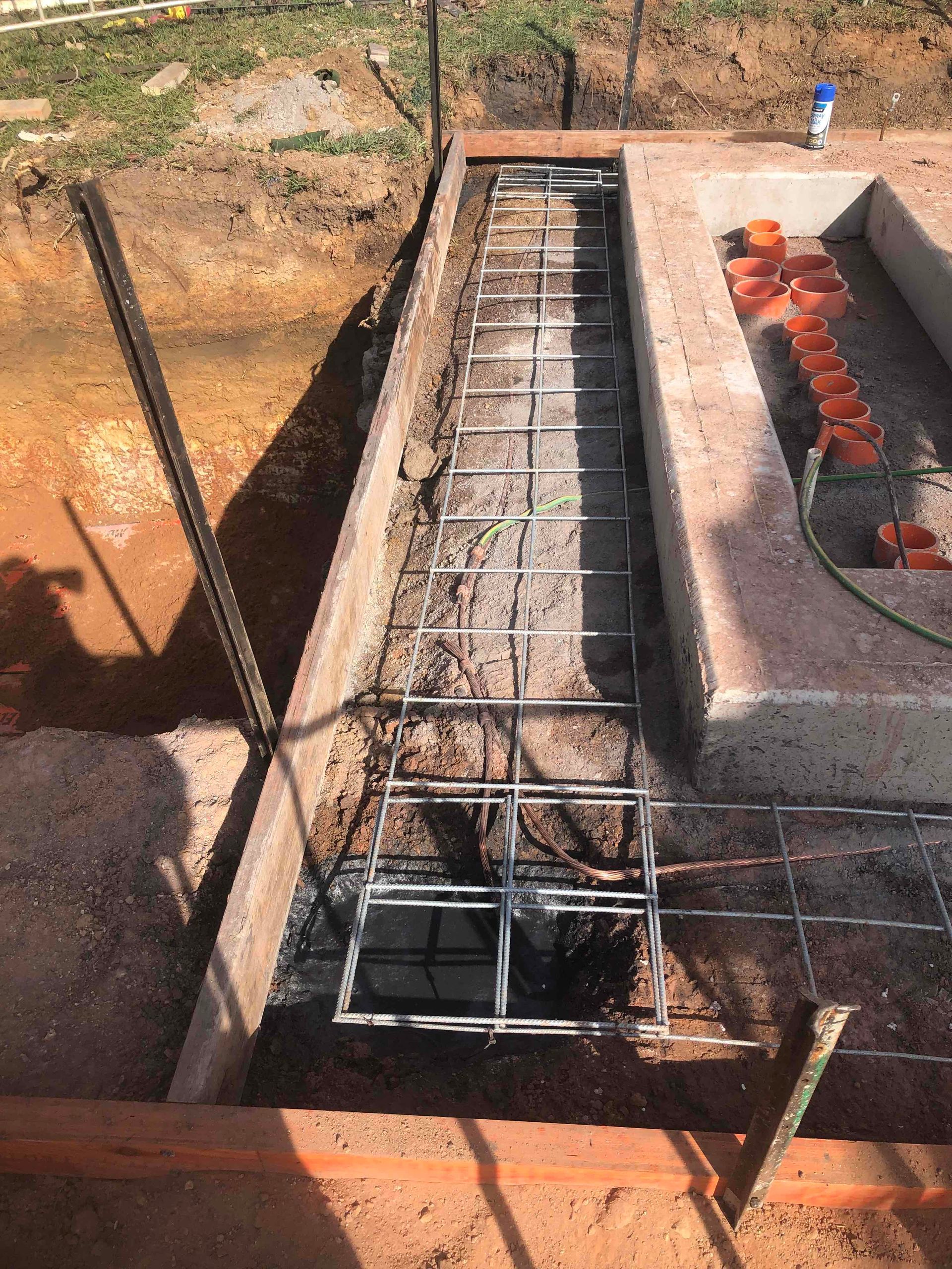 Concrete trench with steel rebar framework under construction beside a concrete structure.