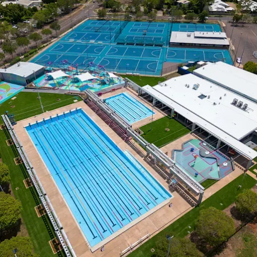 Aerial view of a school sports complex with blue swimming pools and multiple tennis courts