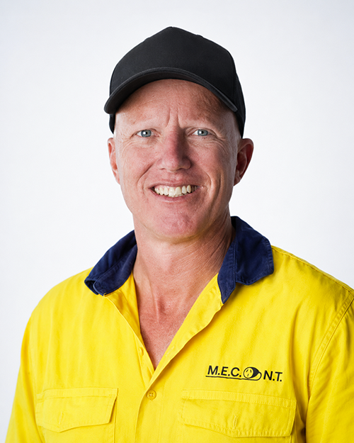 Smiling person in a yellow work shirt and black cap, against a plain light background.