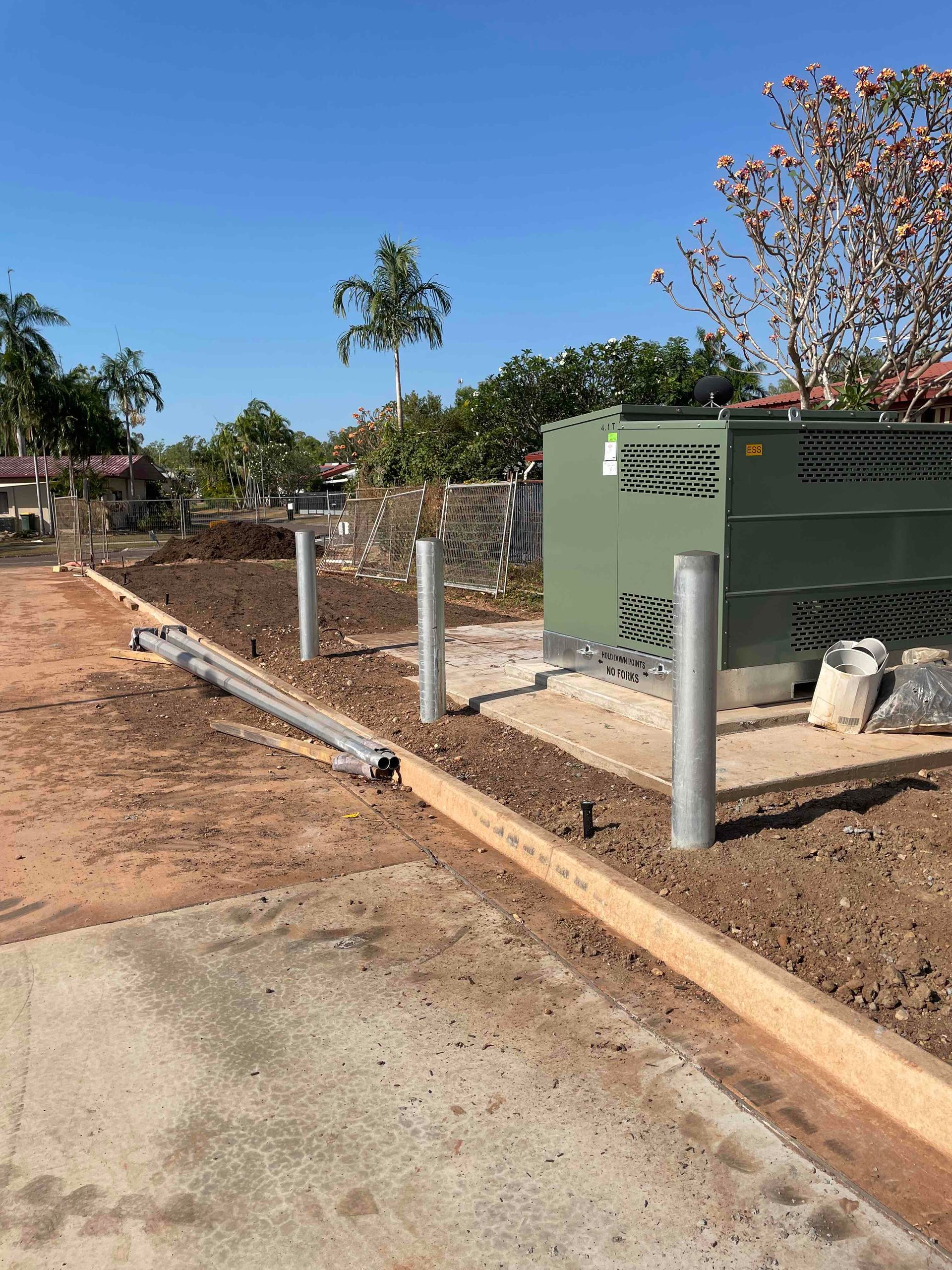Rural roadside with a green utility box, concrete posts, and a dirt path under a clear blue sky