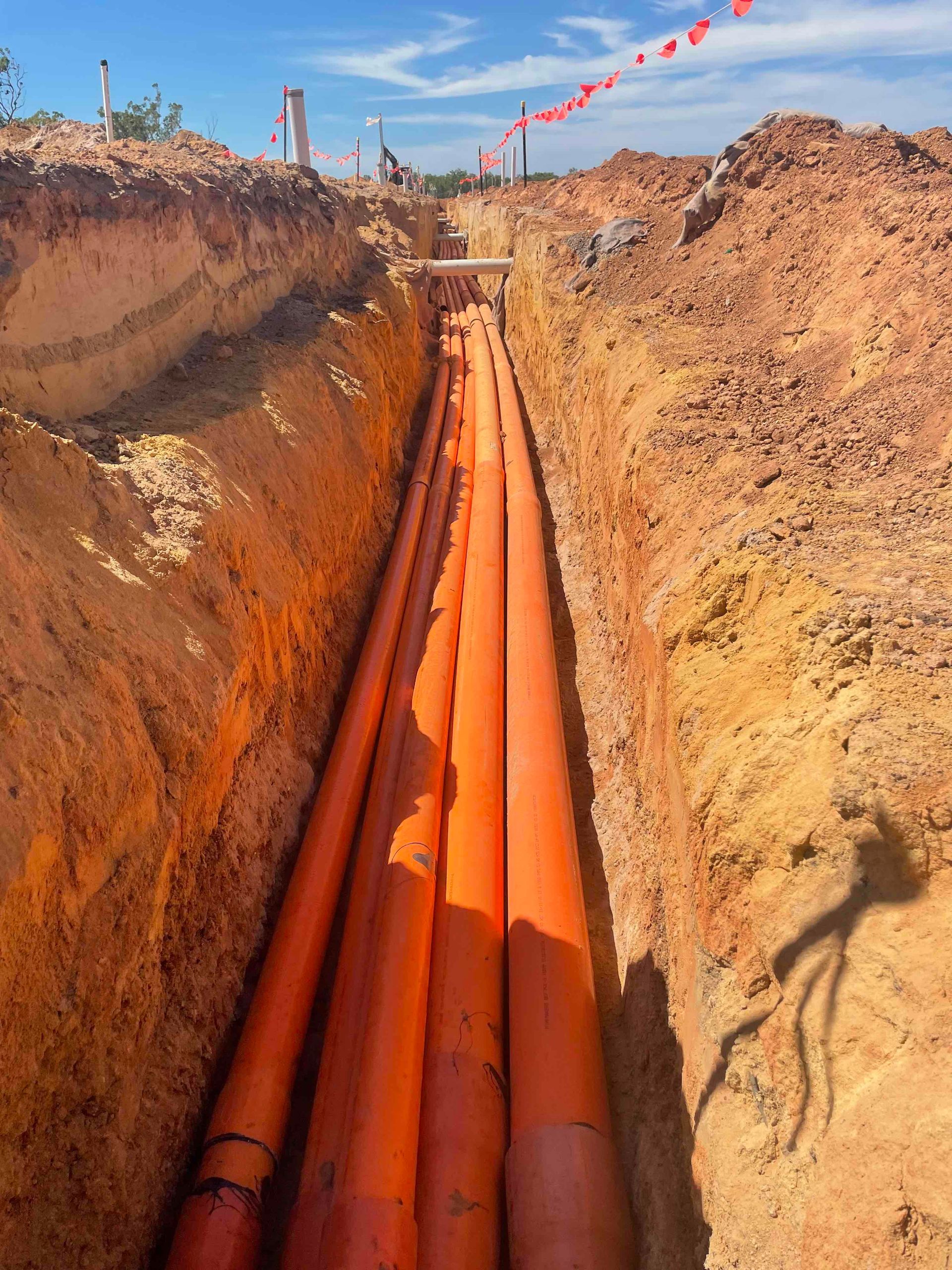 Orange utility pipes laid in a trench at a construction site under a blue sky.