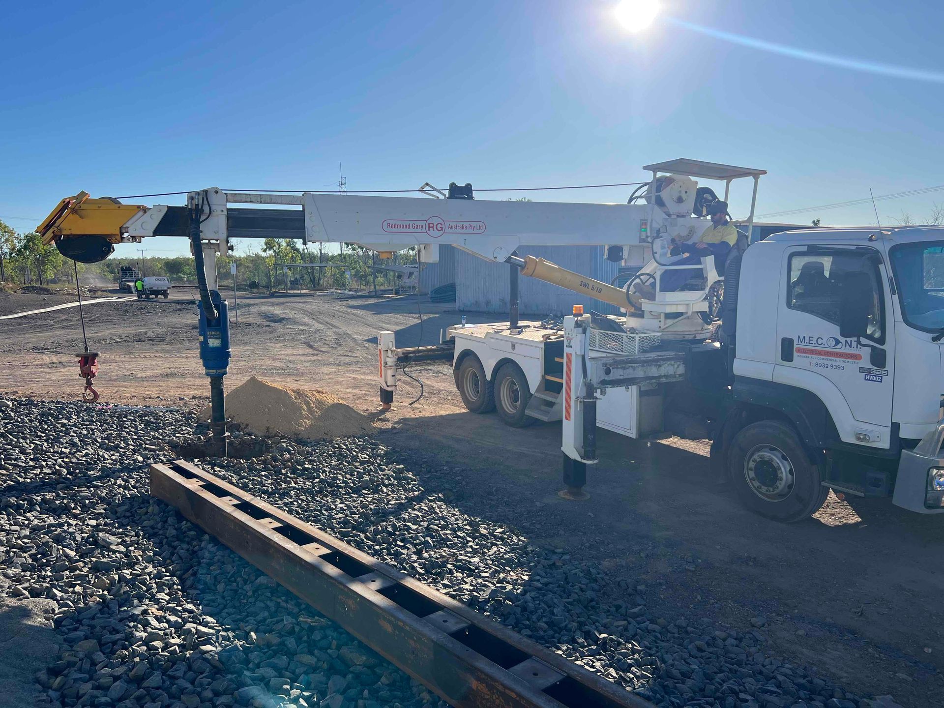Utility truck with bucket lift and worker beside a gravel trench on a sunny construction site