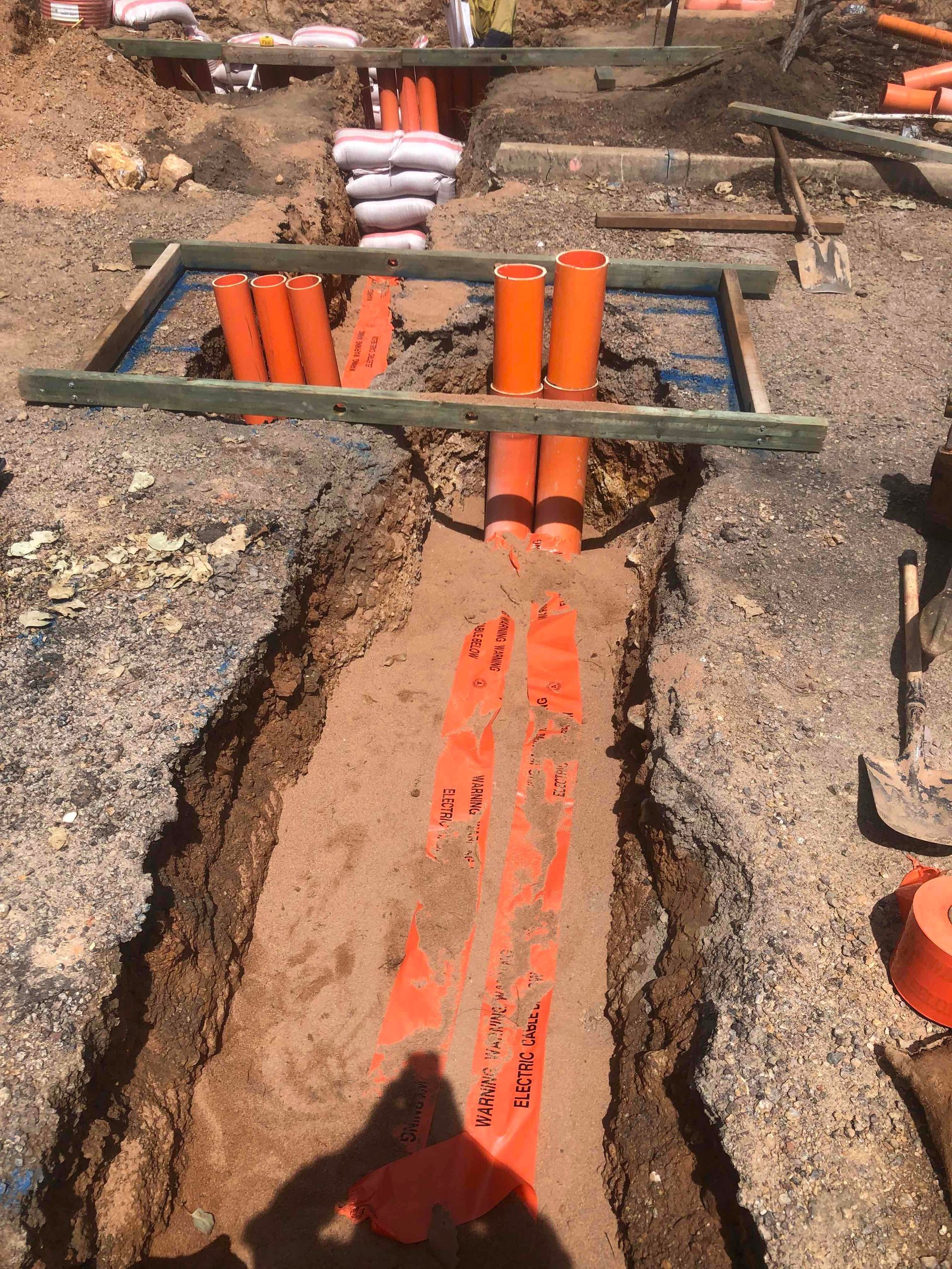 Orange pipes installed in a trench at a construction site, with a metal frame crossing above it.