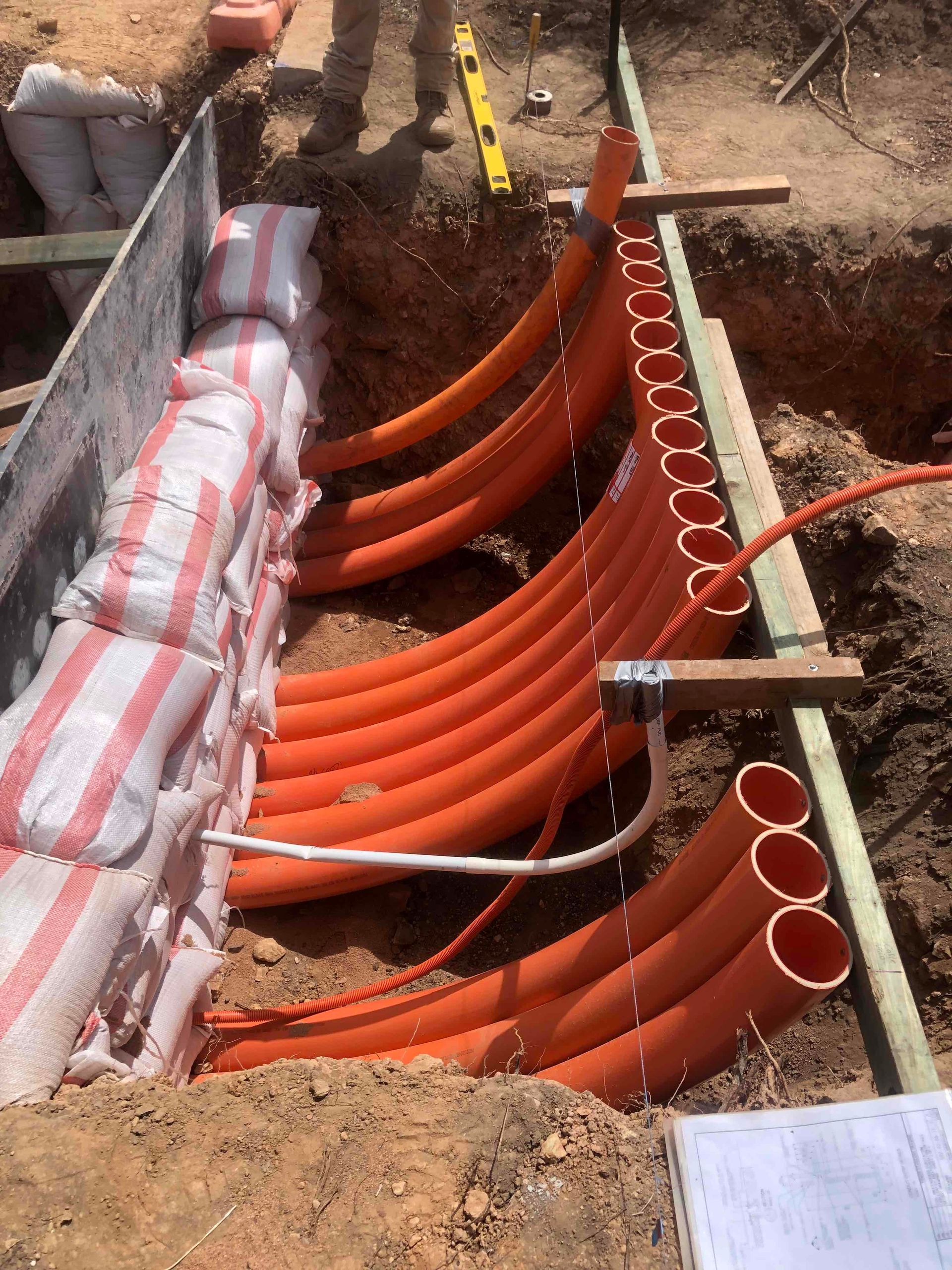 Orange conduit pipes installed in a trench at a construction site, with wrapped cable on the left.