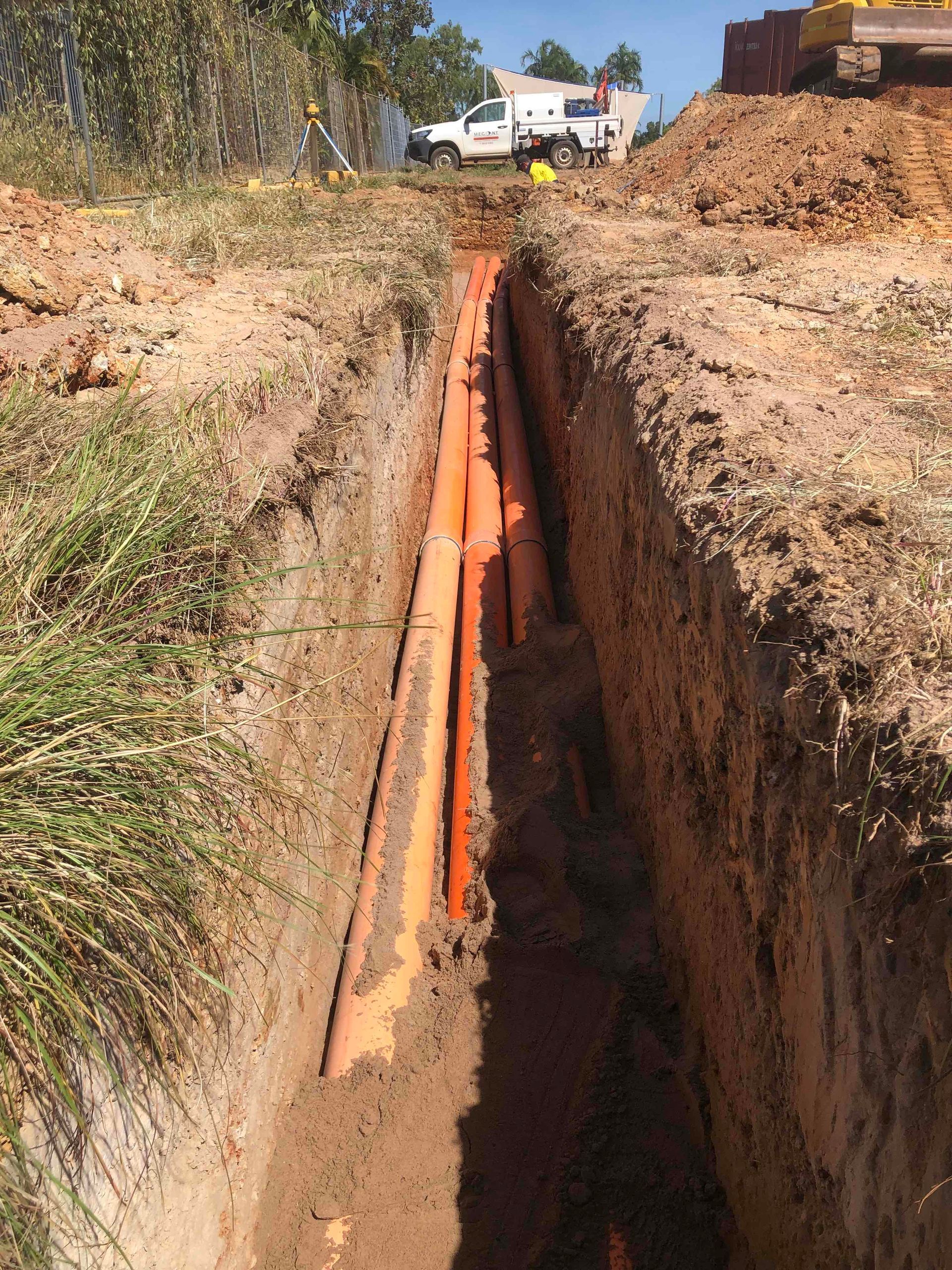 Orange pipeline in a deep trench at a construction site, with dirt piles and machinery in the distance