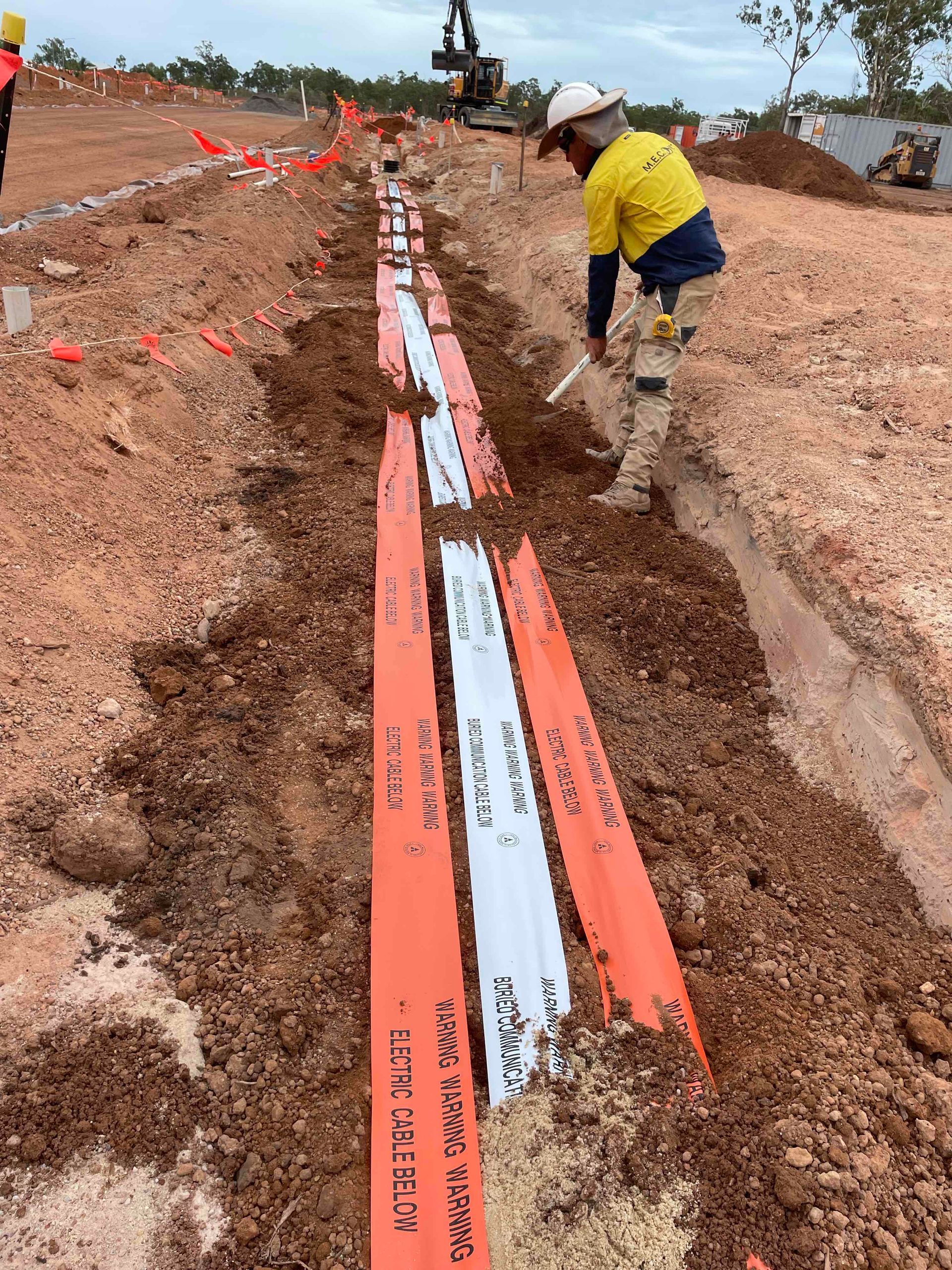 Worker laying orange utility pipes in a muddy trench at a construction site
