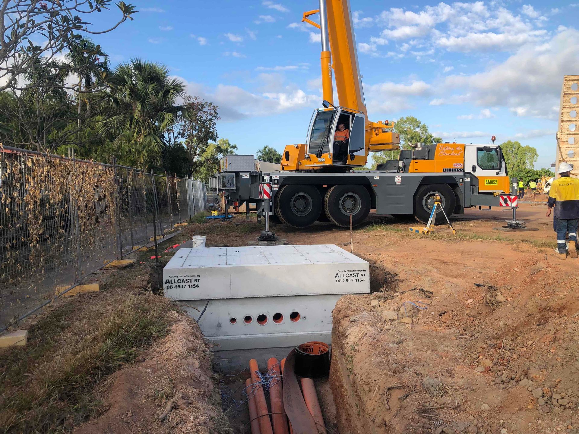Construction site with crane lifting a concrete utility box over an open trench