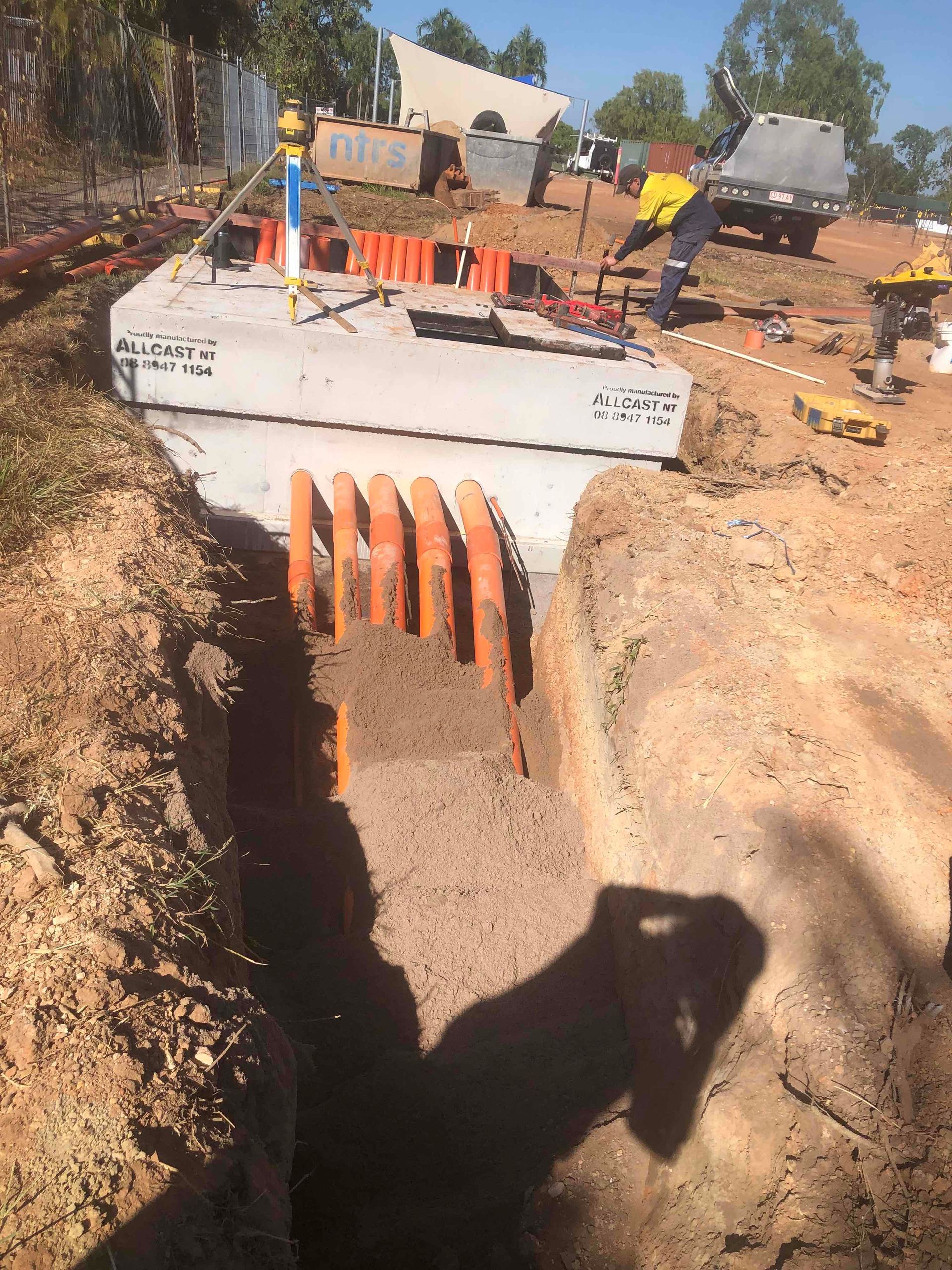 Construction site with orange culvert pipes under a concrete headwall in a trench