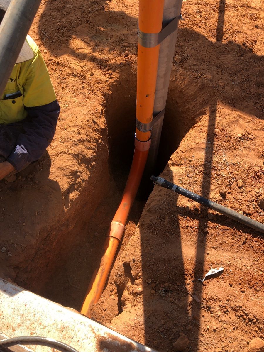 Orange utility pipes in a dirt trench, with a worker partially visible on the left.